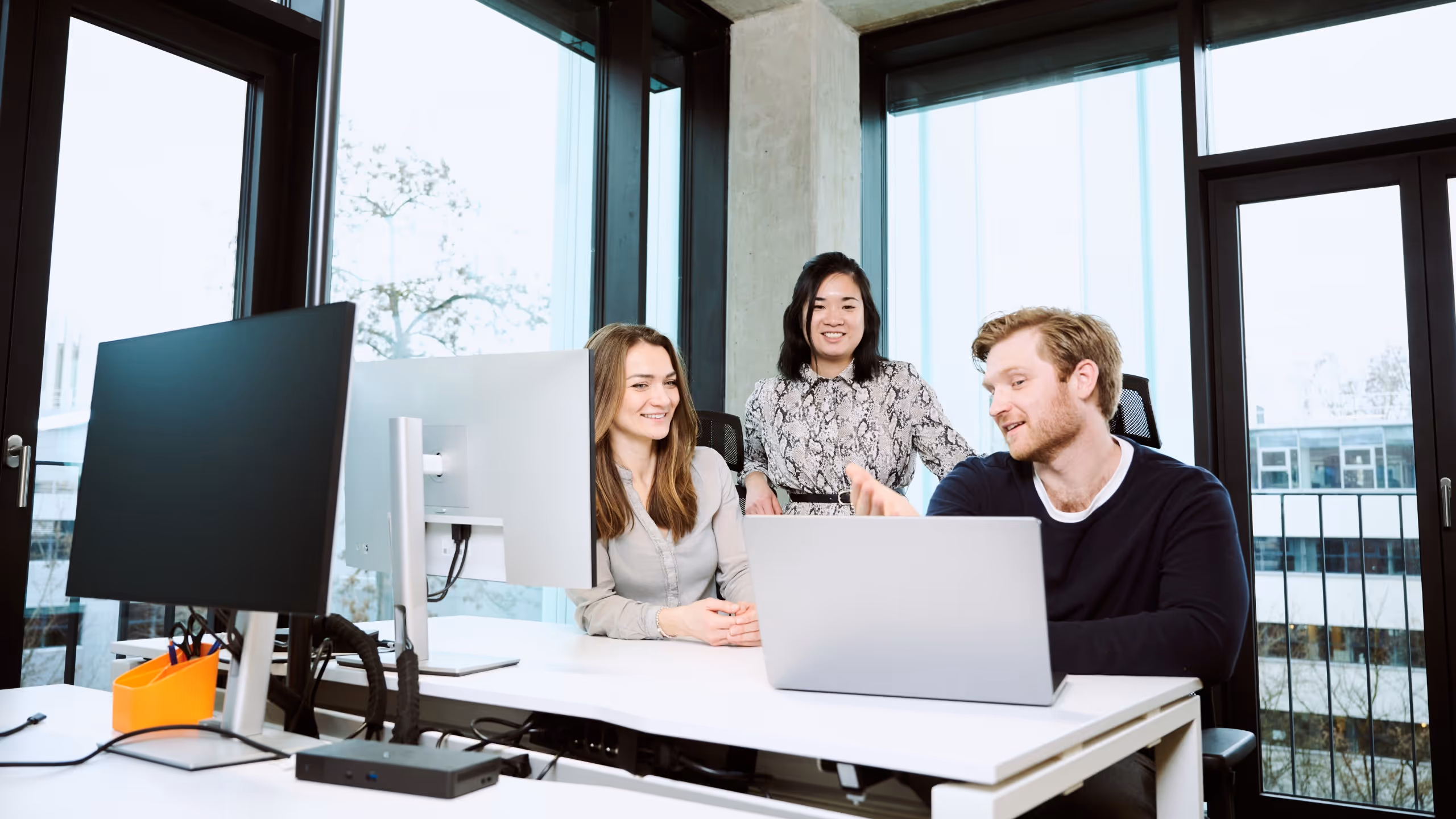 Team collaboration scene in a modern office with three professionals discussing at a workstation, illustrating a productive corporate environment.