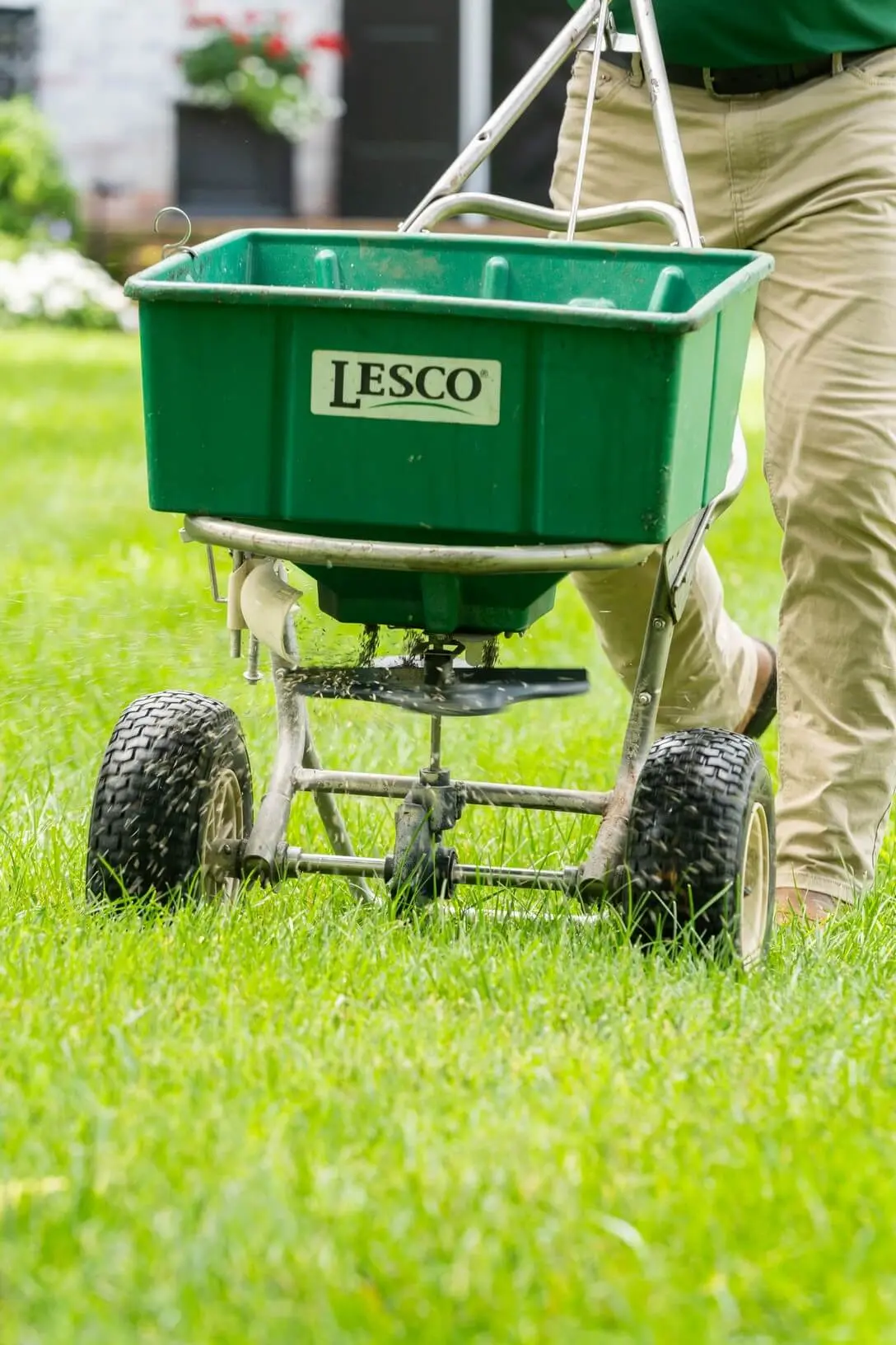 LESCO brand lawn spreader being operated by technician in khaki pants on healthy green residential grass