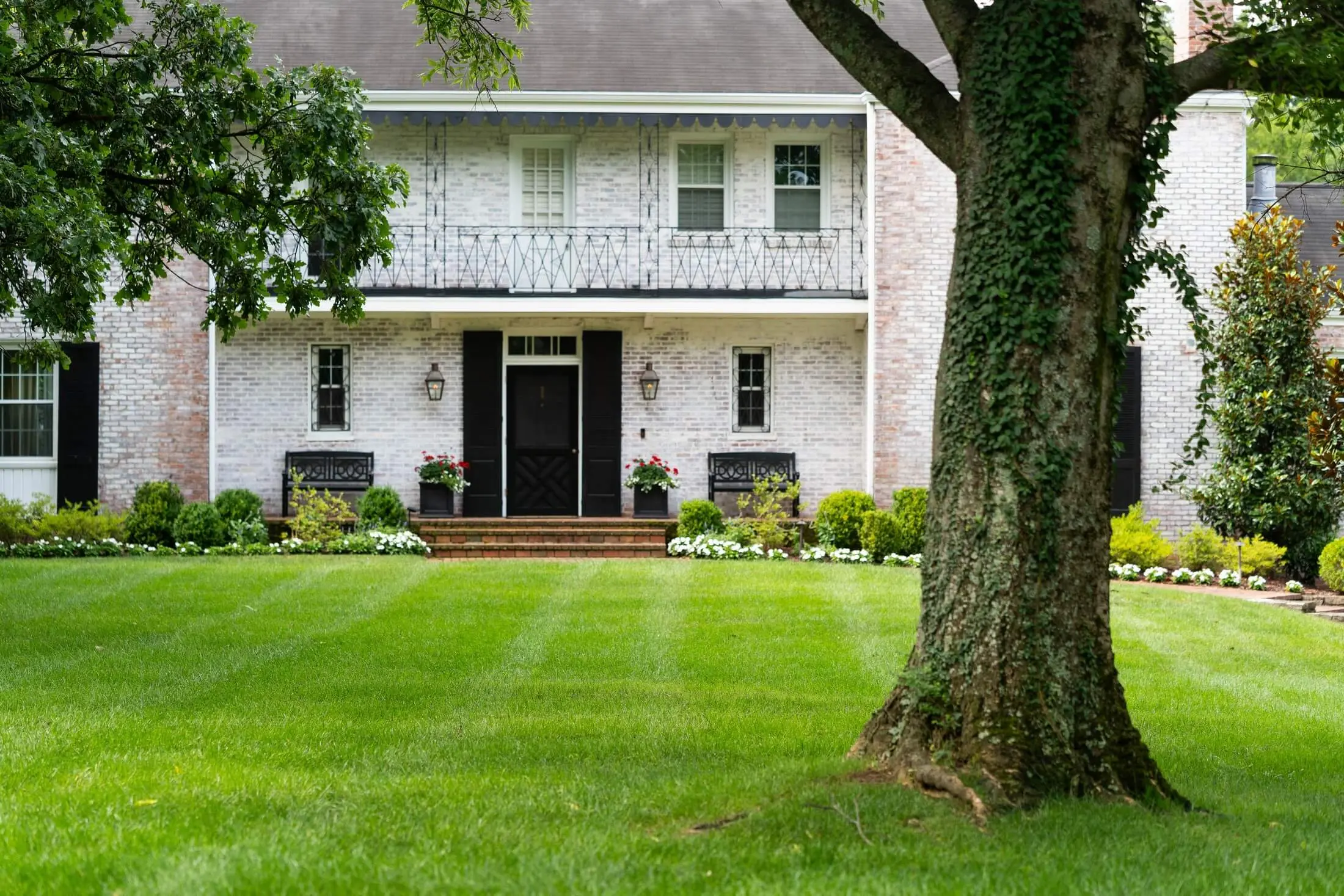 Pristine residential lawn with colonial-style brick home featuring white columns and professional landscaping