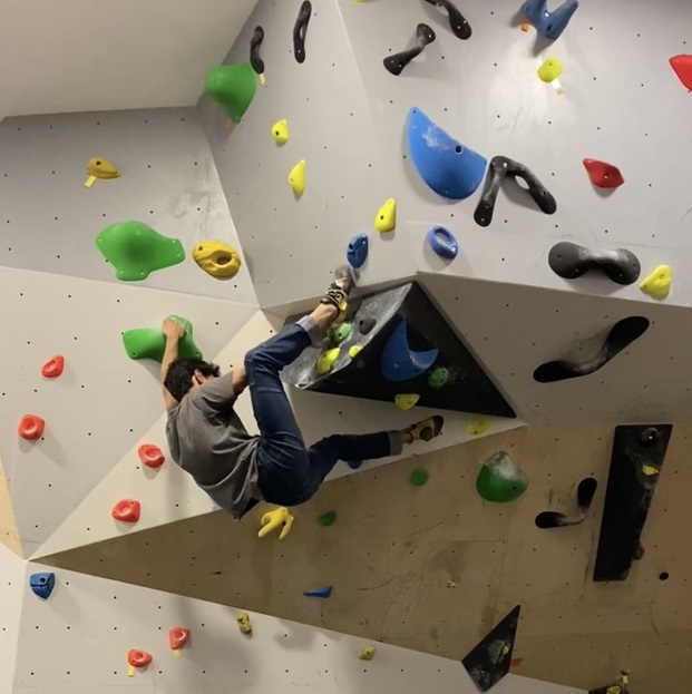 Una persona escalando en el rocódromo. Está colgada de las presas de la pared.