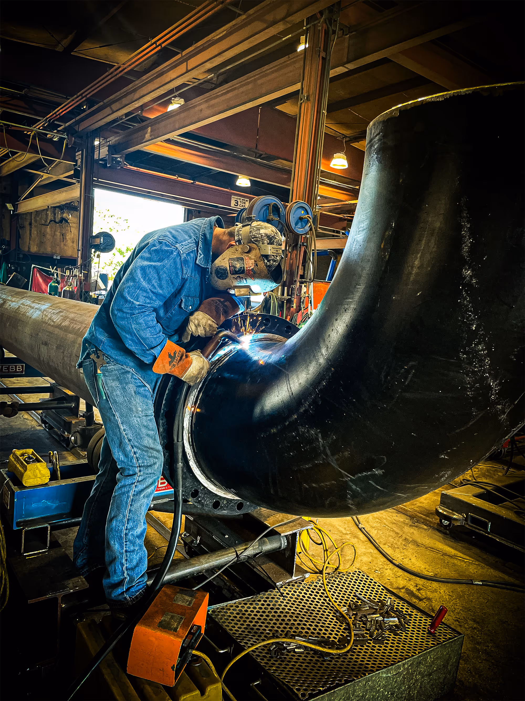 An employee with Freitag-Weinhardt is welding a joint on a curved section of process piping