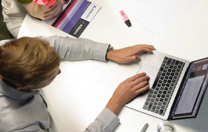 Top-down view of a person using a laptop at a desk with papers and a pink highlighter nearby.