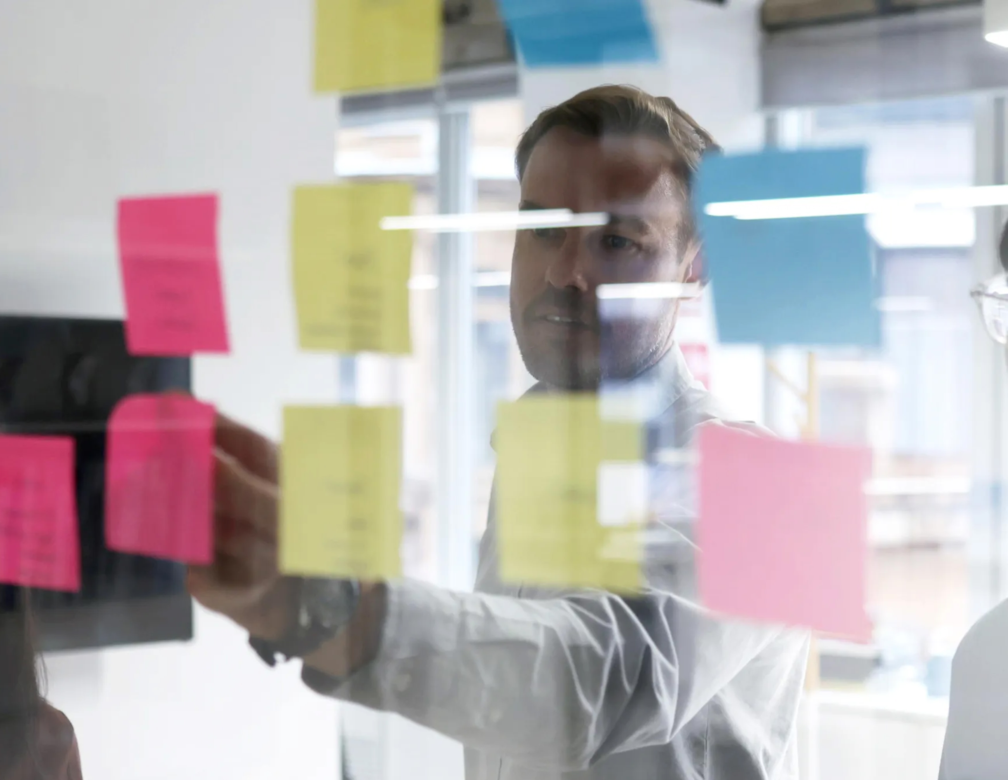 Man in office placing colorful sticky notes on glass wall during a brainstorming session.