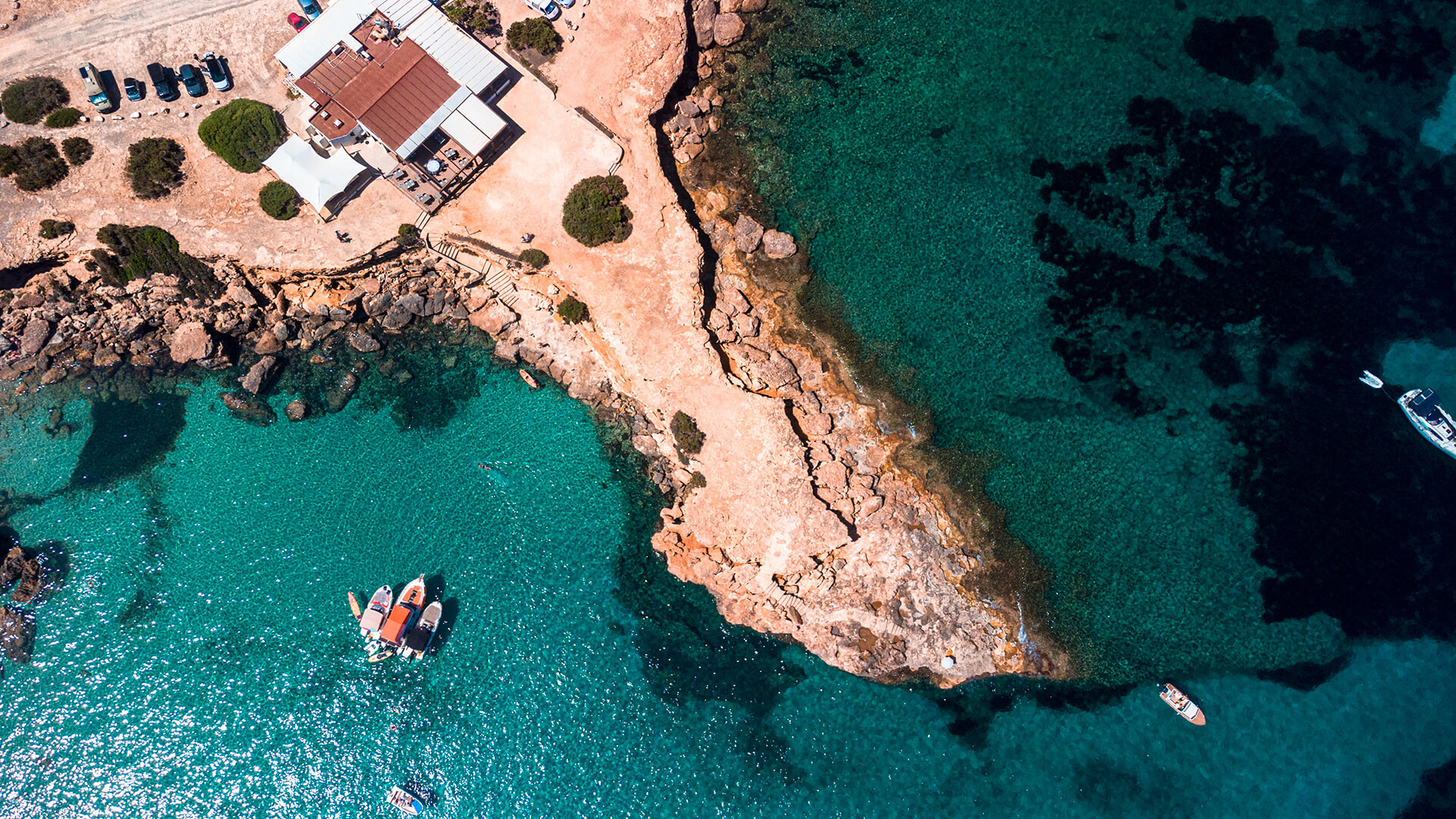 Aerial view of a rocky cove with clear turquoise water and boats