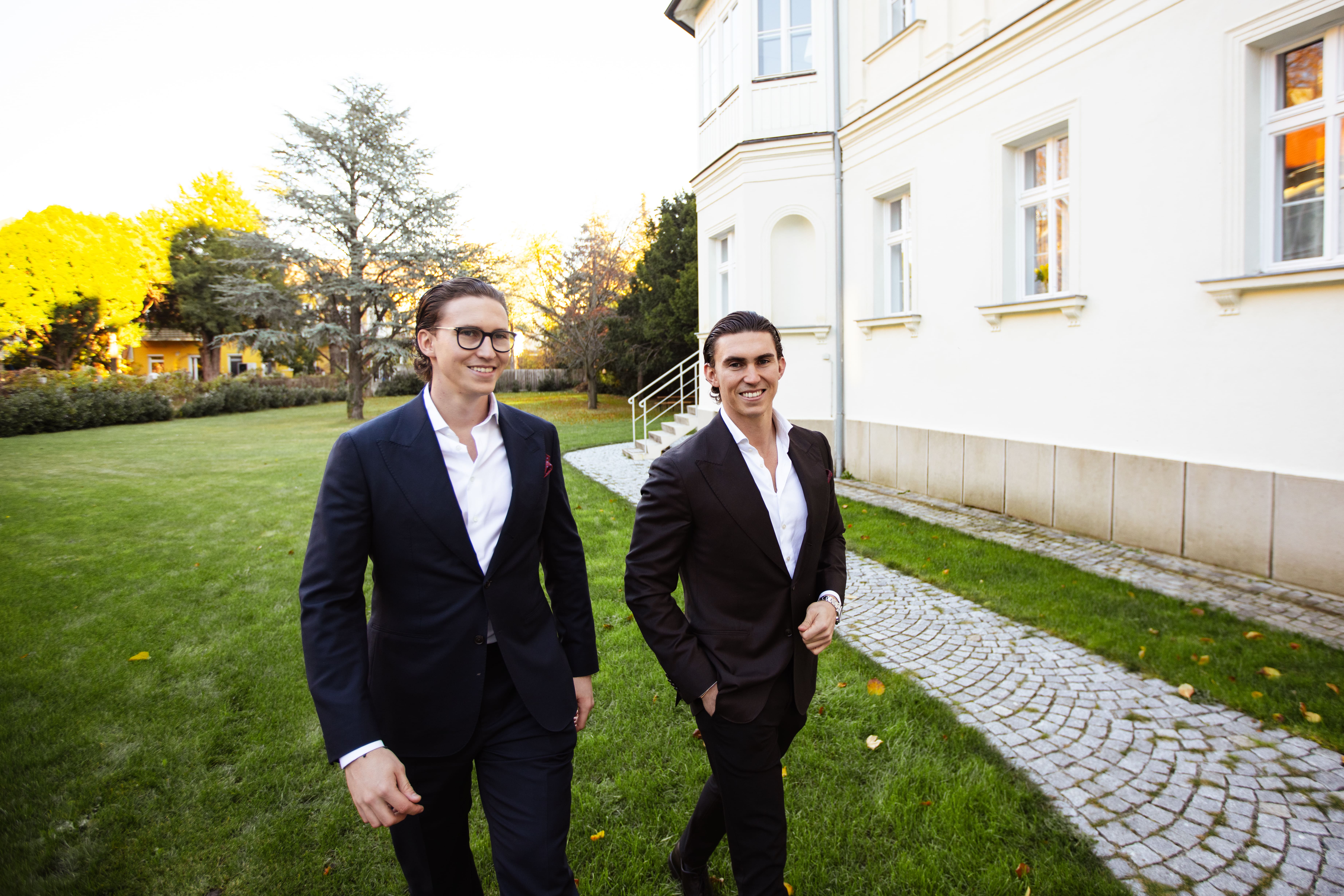 Man in white shirt and black pants taking a photo with a camera in a modern kitchen with white cabinets and wooden floor.
