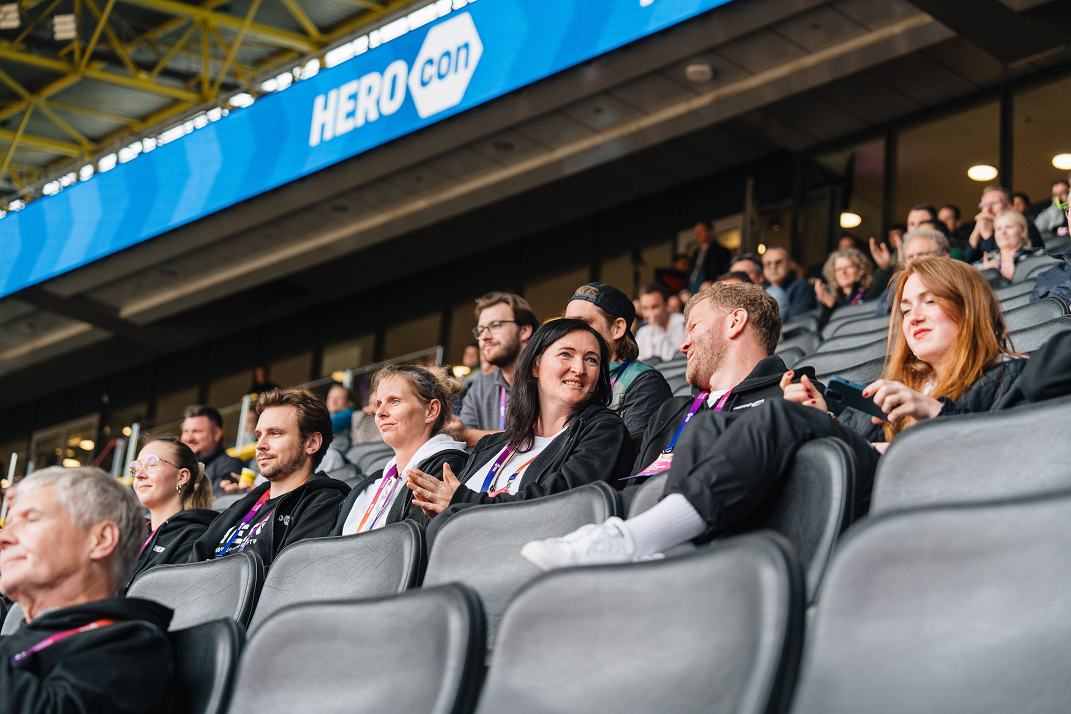 Menschen sitzen in einem Stadion und unterhalten sich während der HEROcon.