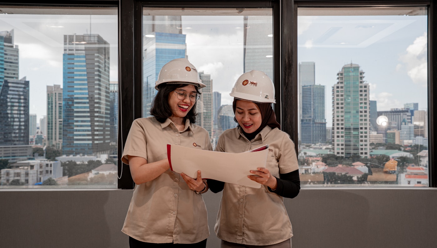 Two engineers in hard hats reviewing blueprints indoors
