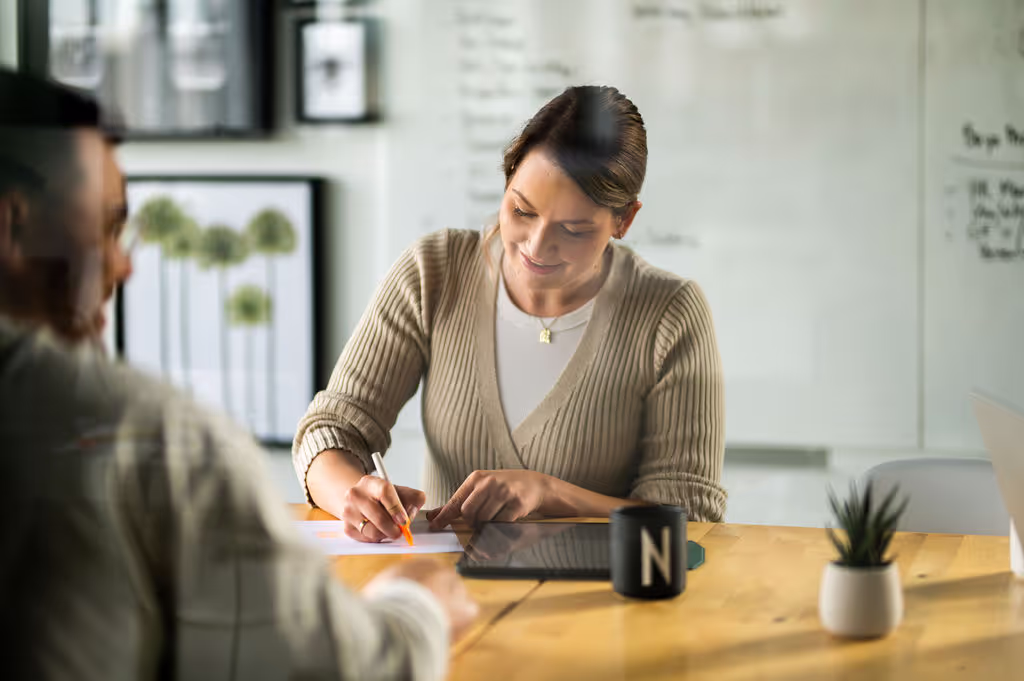 Frau mit Laptop und Notizblock im Gespräch mit zwei Personen in moderner Büroumgebung. Symbolbild für Beratung, Teamwork oder UX-Interview.