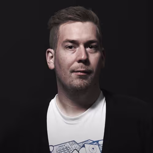 Porträt eines Mannes mit ernster Miene, dunklem Hintergrund und weißem T-Shirt unter einer schwarzen Jacke. Studioaufnahme mit starker Licht-Schatten-Kontur.

