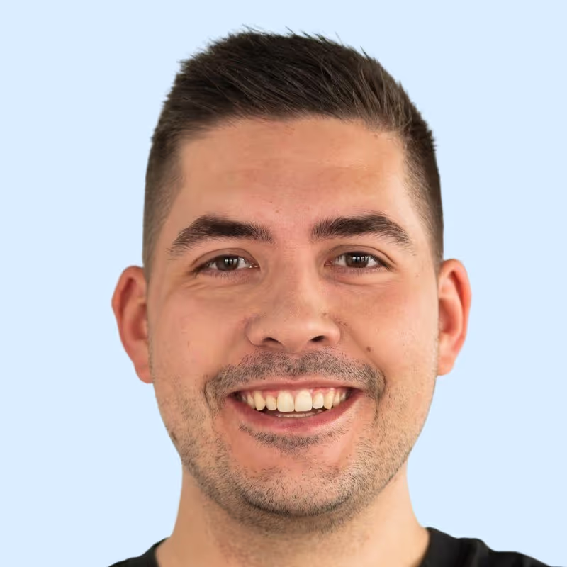 Porträt eines lächelnden Mannes mit hellem Hintergrund, dunklen Pullover und direktem Blick in die Kamera.