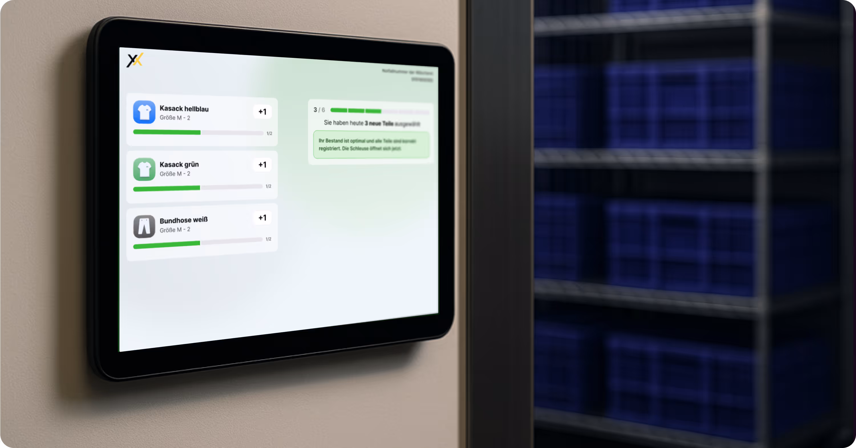 Digitales Wanddisplay mit der modernen Texxeo-Software zeigt eine übersichtliche Bestandsanzeige für Berufskleidung, darunter Kasacks in verschiedenen Farben und Bundhosen. Alle Einträge sind grün markiert mit dem Status „verfügbar“. Rechts im Hintergrund sind Regalfächer mit blauen Lagerkisten sichtbar. Symbolbild für transparente Lagerverwaltung und intuitive textile Ausgabe im Pflegealltag.