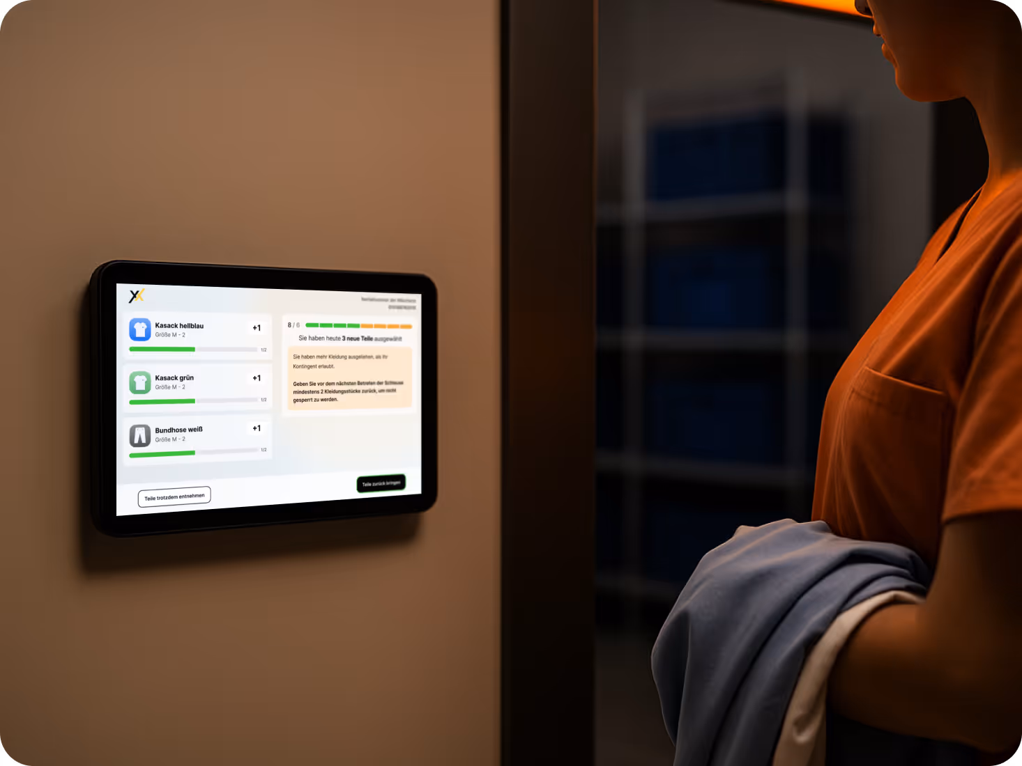 Moderne Benutzeroberfläche der Texxeo-Software an einem Wand-Tablet. Eine Pflegekraft in orangefarbener Kleidung steht davor mit frisch gefalteter Wäsche im Arm. Das Interface zeigt eine strukturierte, visuell reduzierte Übersicht mit klaren Statusanzeigen und Auswahlmöglichkeiten. Symbolbild für benutzerfreundliches UI-Redesign in der textilen Versorgung.