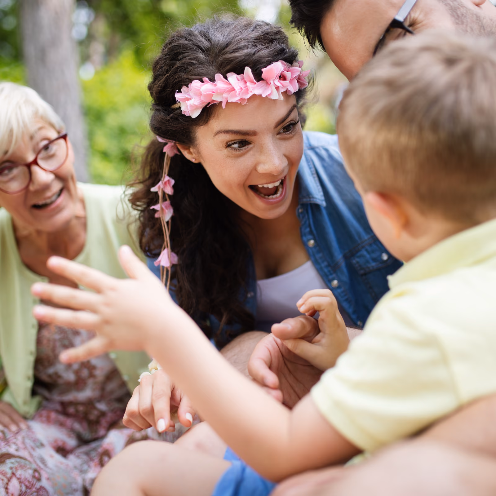 Smiling multi-generational family playing and interacting outdoors with a young boy reaching out.