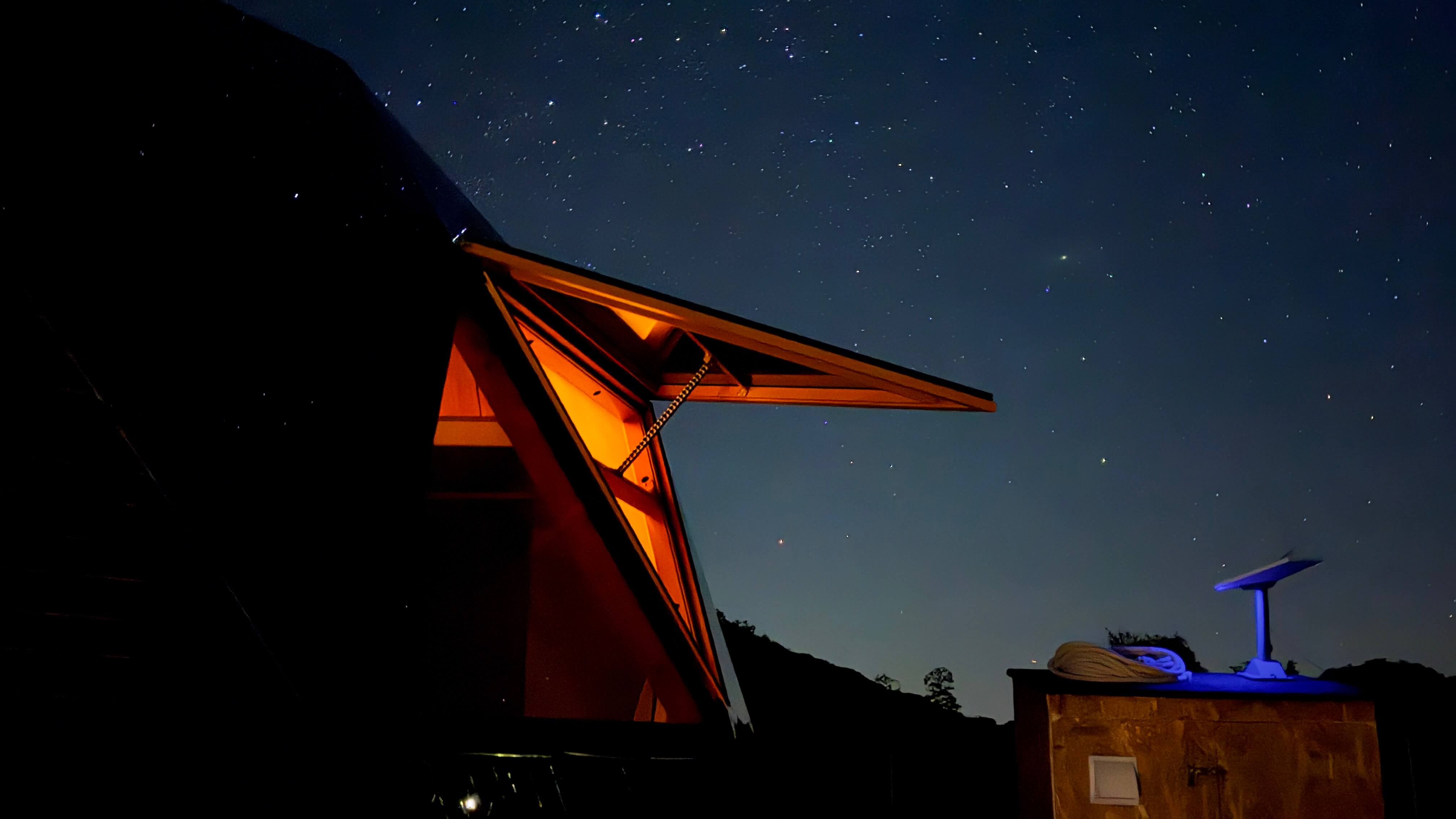 Night sky full of stars above the Solar Dome Retreat, Samothraki, with the dome's roof window propped open and warm light inside