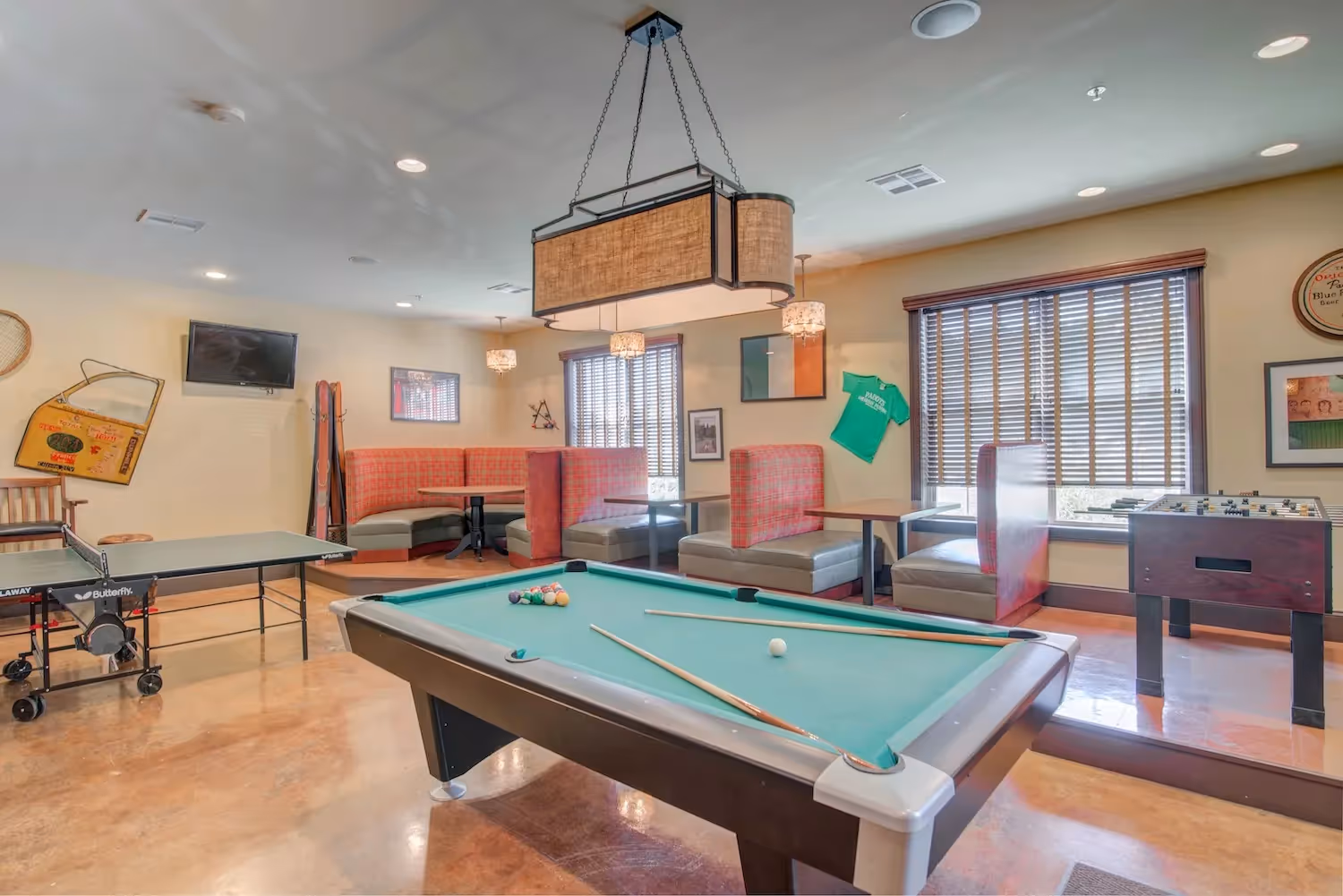 Vibrant game room at The Grand at Lake Sheri, Valdosta, GA, with a billiards table, foosball, and comfortable booth seating.