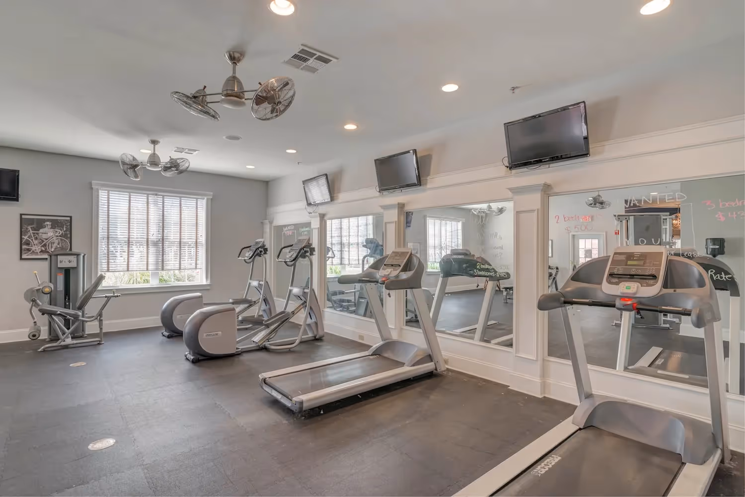 Well-equipped gym at The Grand at Lake Sheri, Valdosta, GA, showing cardio machines, weight benches, and mirrored walls.