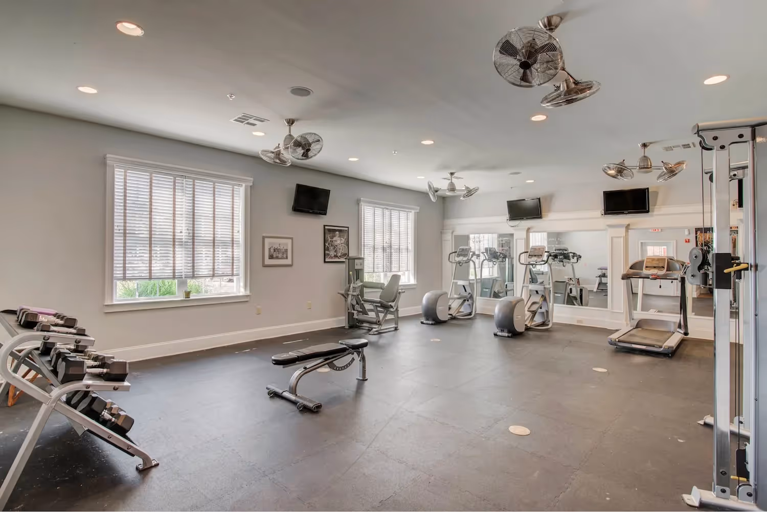 Well-equipped gym at The Grand at Lake Sheri, Valdosta, GA, showing cardio machines, weight benches, and mirrored walls.