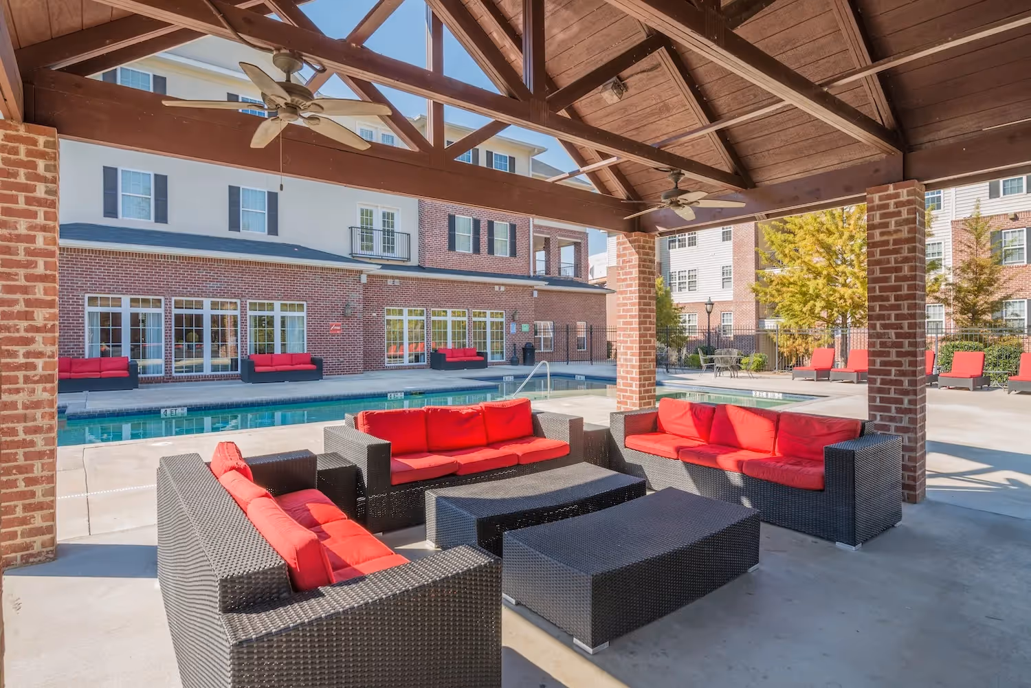 Covered outdoor lounge area with wicker seating and red cushions next to the swimming pool at The Grand at Lake Sheri, Valdosta, GA.