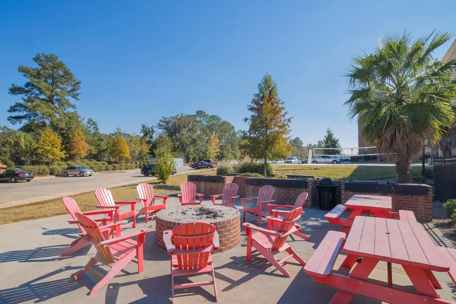 Outdoor brick fire pit surrounded by red Adirondack chairs and picnic tables at The Grand at Lake Sheri in Valdosta, GA.