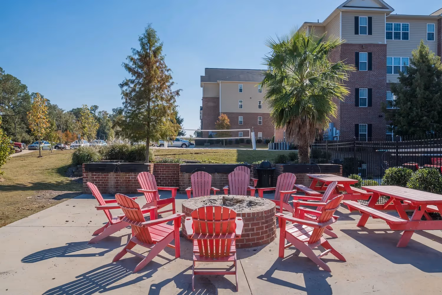 Outdoor fire pit area with red Adirondack chairs and picnic tables at The Grand at Lake Sheri in Valdosta, GA, perfect for social gatherings.