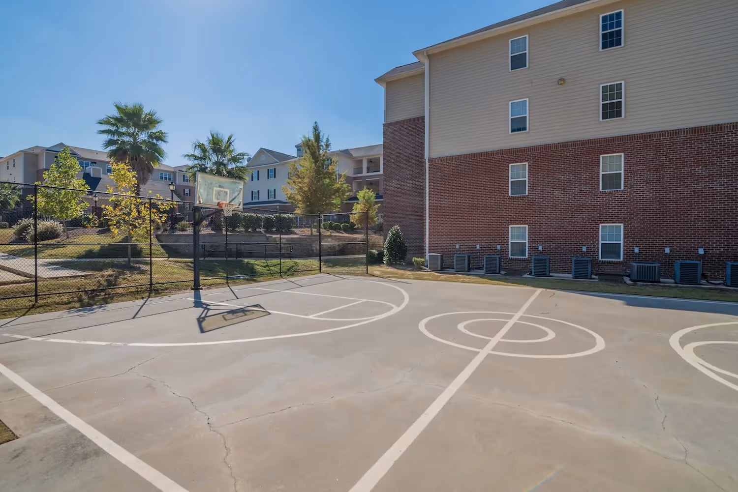 Outdoor basketball court at The Grand at Lake Sheri, Valdosta, GA, with apartment buildings in the background, offering resident recreation.