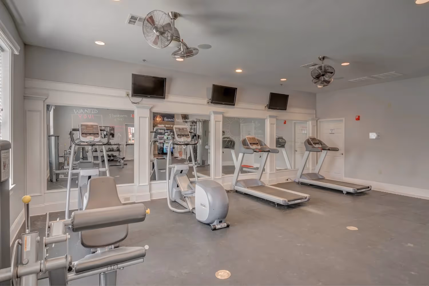 Fitness center at The Grand at Lake Sheri in Valdosta, GA, featuring a variety of cardio machines, weights, mirrors, and ceiling fans.