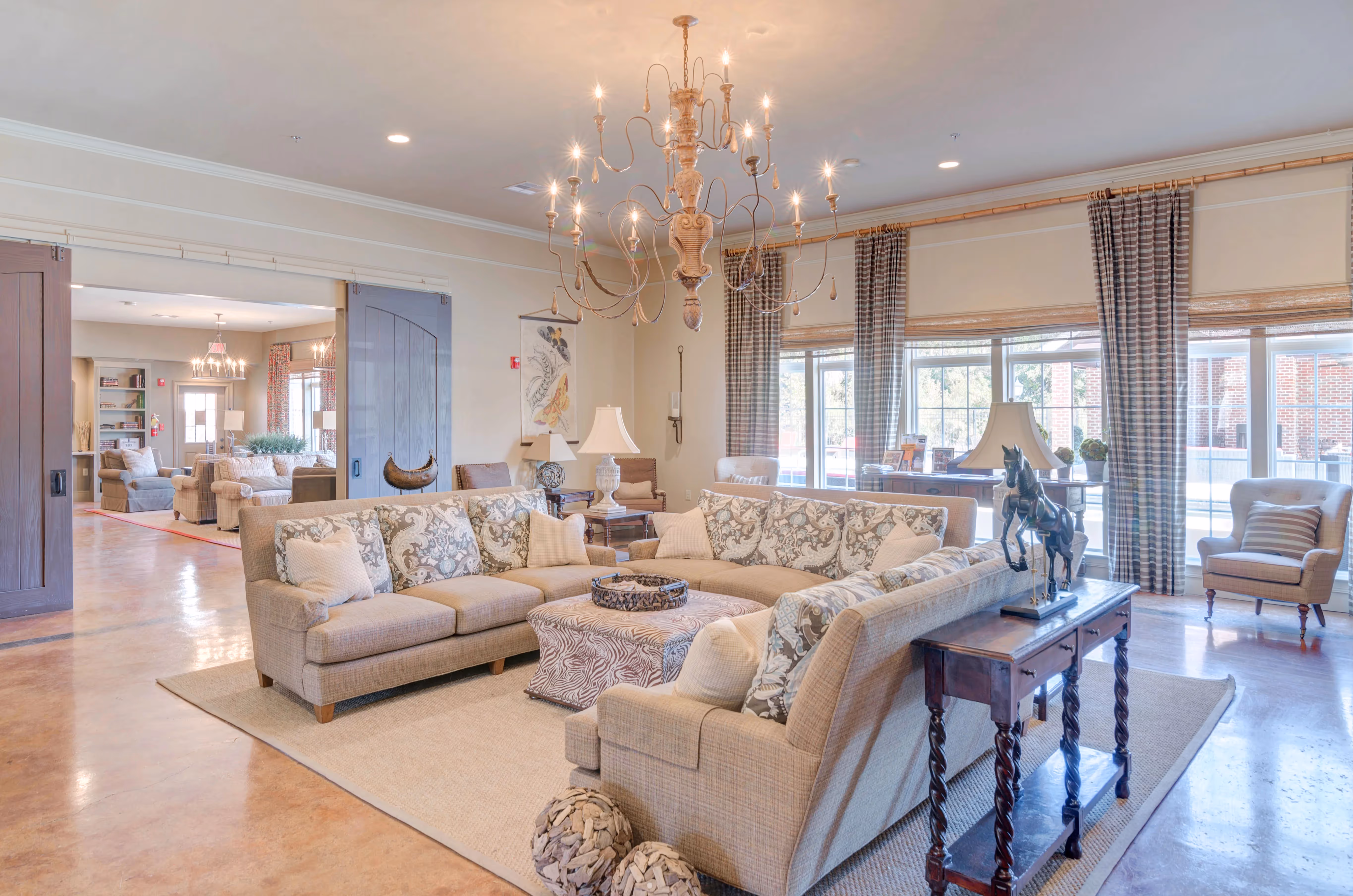 Luxurious living room in the clubhouse at The Grand at Lake Sheri in Valdosta, GA, with elegant sofas, a large chandelier, and ample seating.
