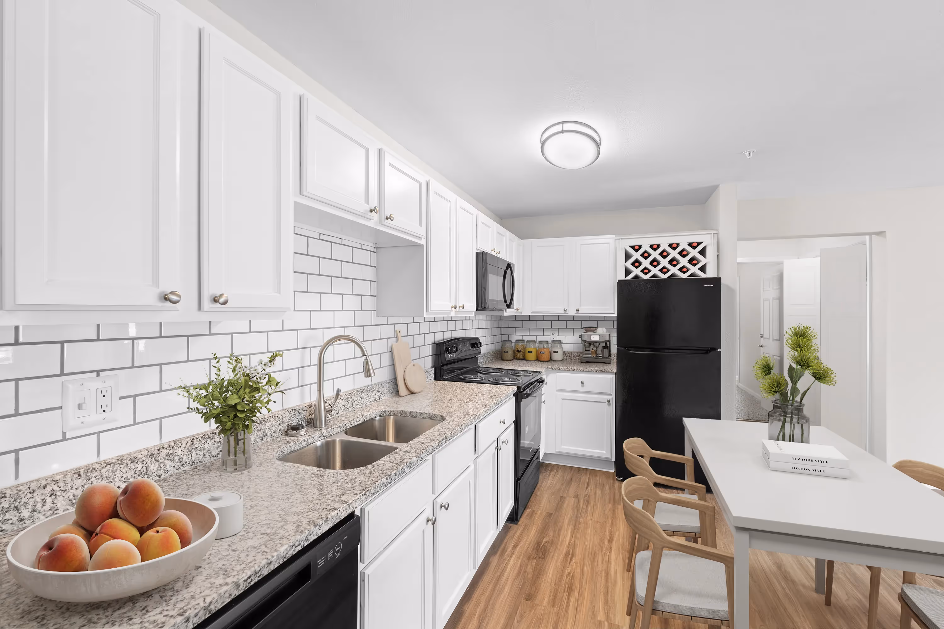 Bright apartment kitchen at The Grand at Lake Sheri, Valdosta, GA, featuring white shaker cabinets, granite countertops, subway tile backsplash, and a dining area.