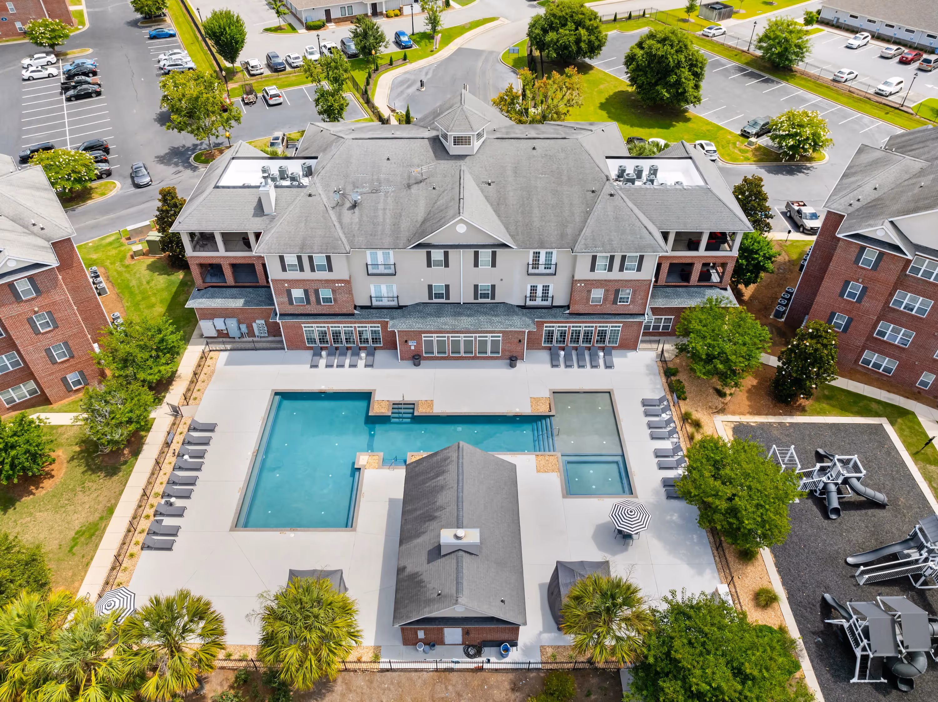 Aerial view of The Grand at Lake Sheri apartment complex in Valdosta, GA, showcasing the large swimming pool, courtyard, and surrounding buildings.
