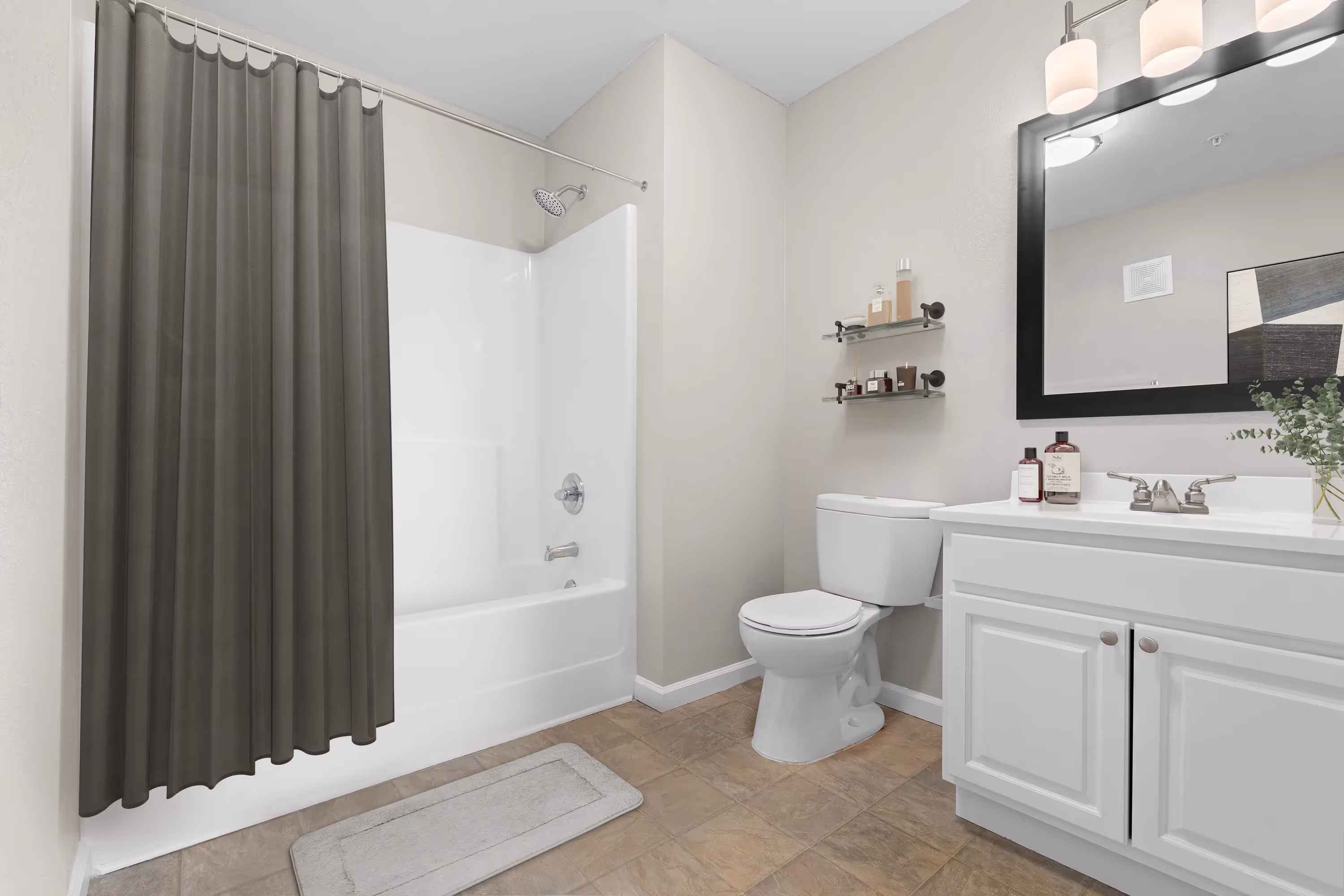 Modern bathroom with white vanity, dark framed mirror, toilet, and a bathtub with a gray shower curtain at The Grand at Lake Sheri in Valdosta, GA.