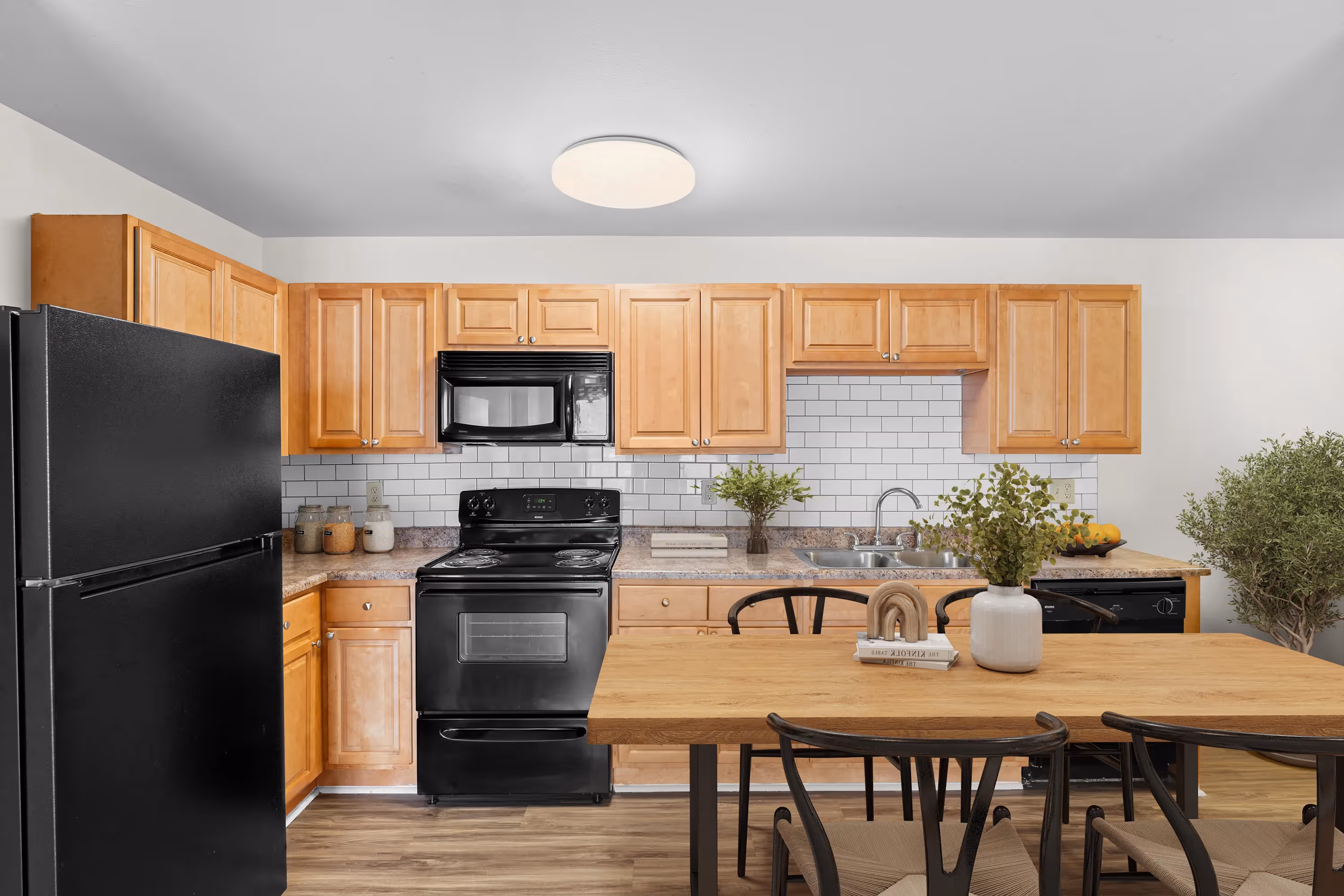 Apartment kitchen with wooden cabinets, white subway tile backsplash, black appliances, and an adjacent dining table at The Grand at Lake Sheri, Valdosta, GA.