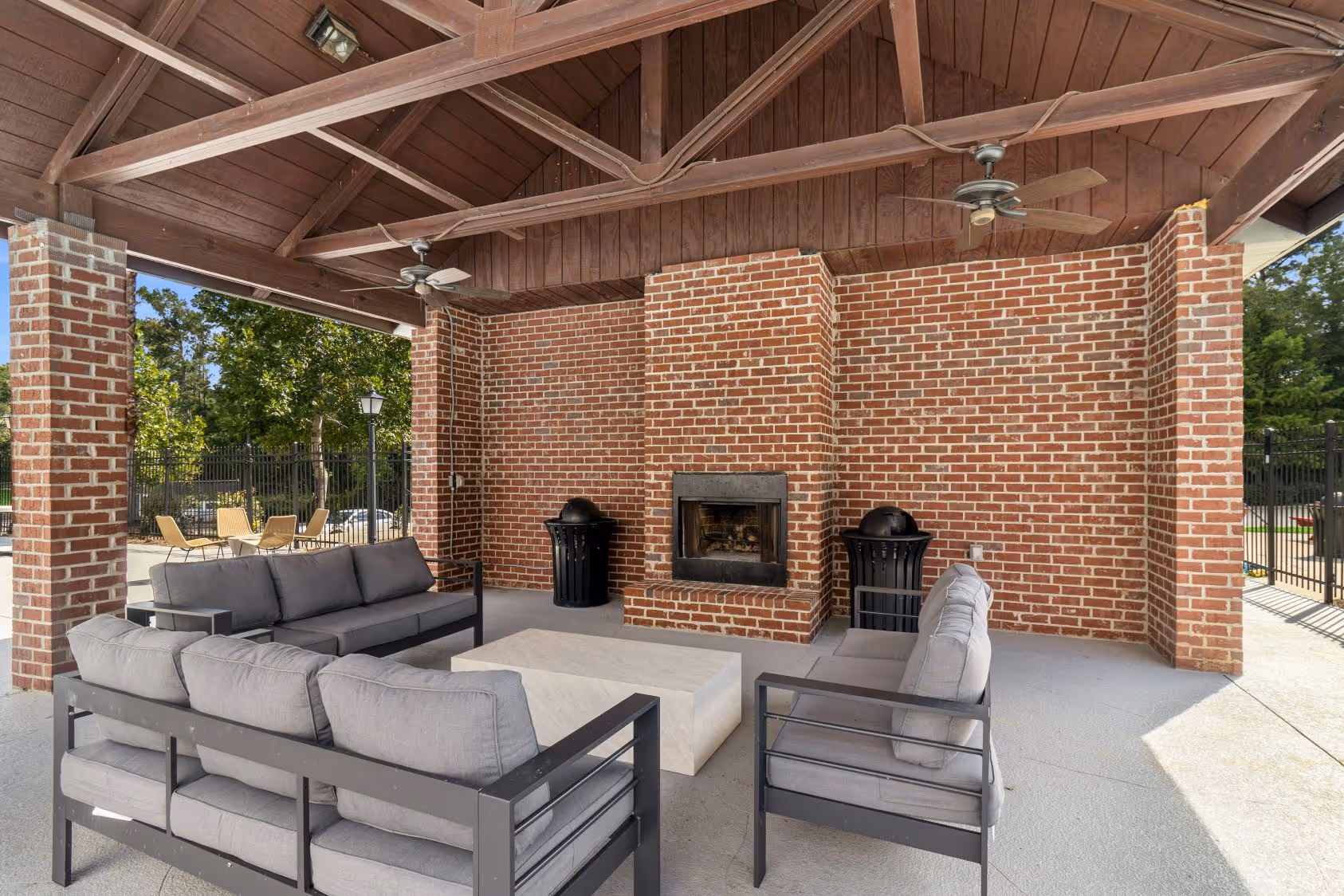 Covered outdoor lounge area with wicker seating and red cushions next to the swimming pool at The Grand at Lake Sheri, Valdosta, GA.
