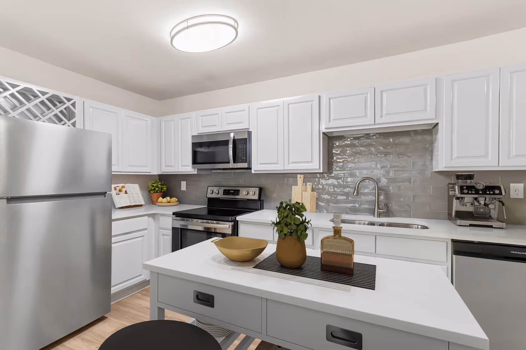Bright apartment kitchen at The Grand at Lake Sheri, Valdosta, GA, featuring white shaker cabinets, granite countertops, subway tile backsplash, and a dining area.