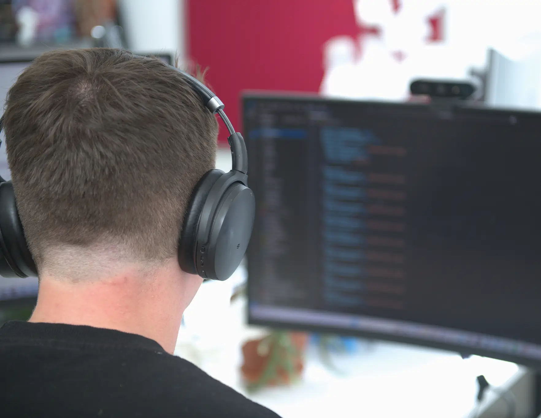 Rear view of a person wearing black headphones looking at a computer screen displaying code.