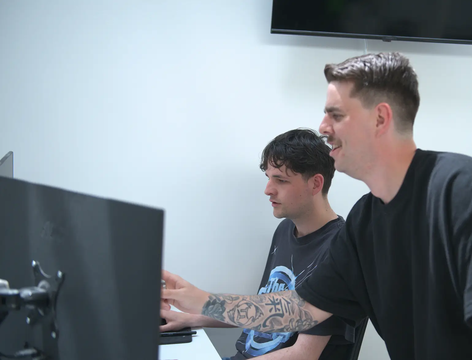 Two men collaborating in an office, one pointing at a computer screen while the other watches attentively.