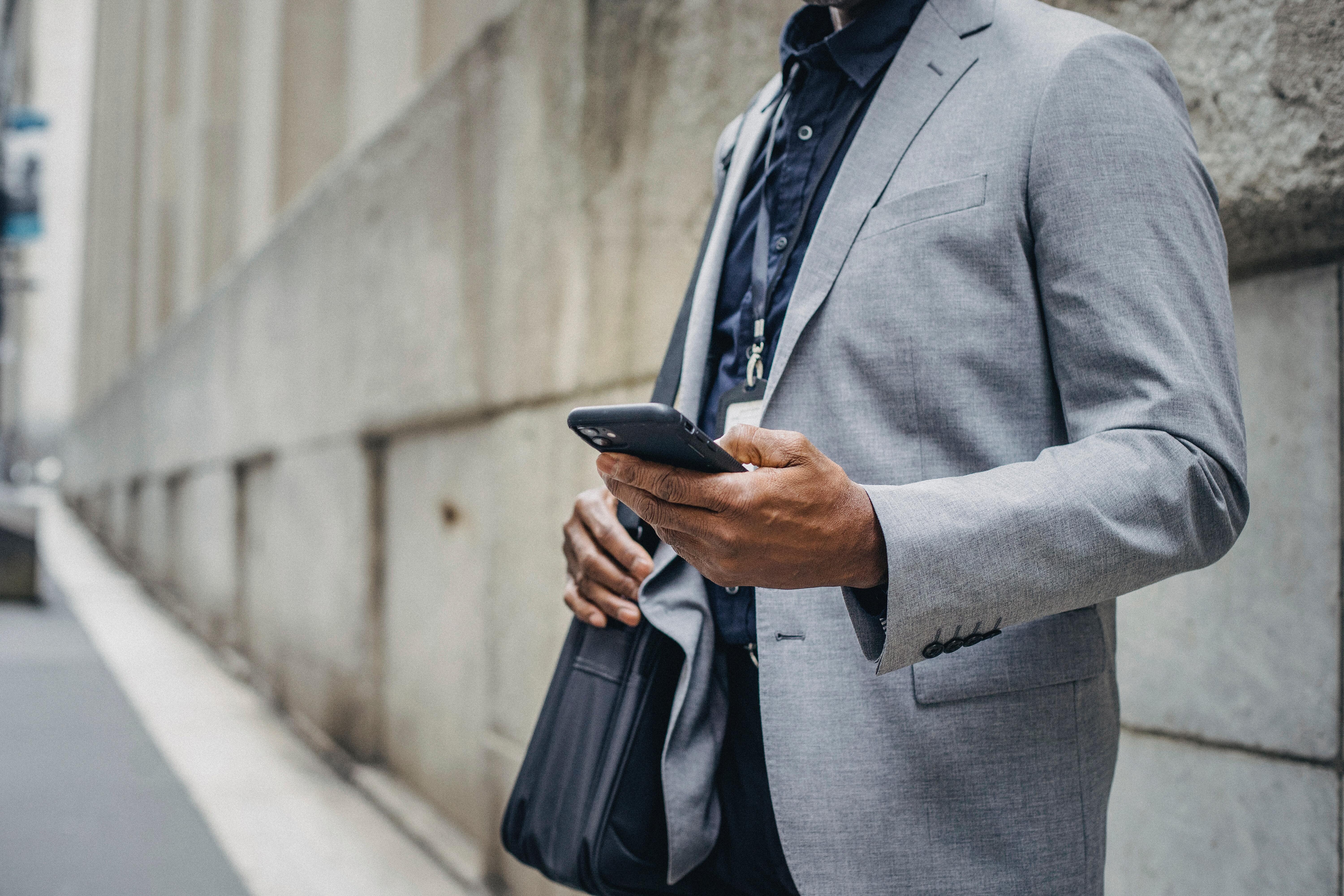 Professional in a suit using a smartphone to manage m360 business messaging while on the go.