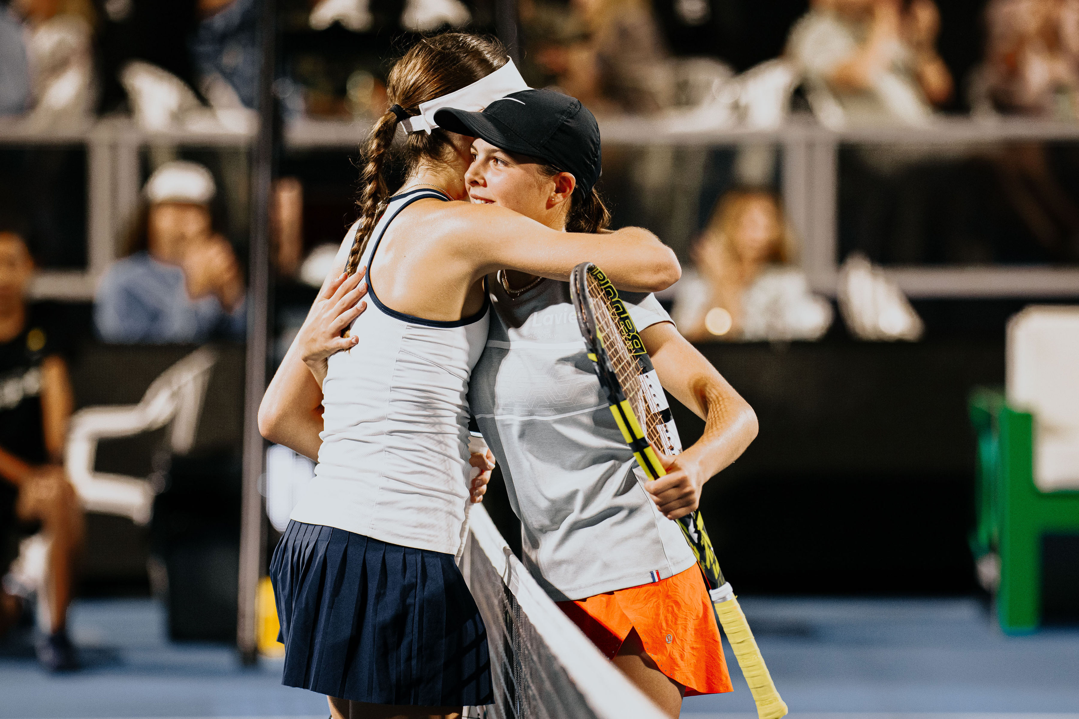Two junior players hugging at the net after the Road to the ASB Classic final