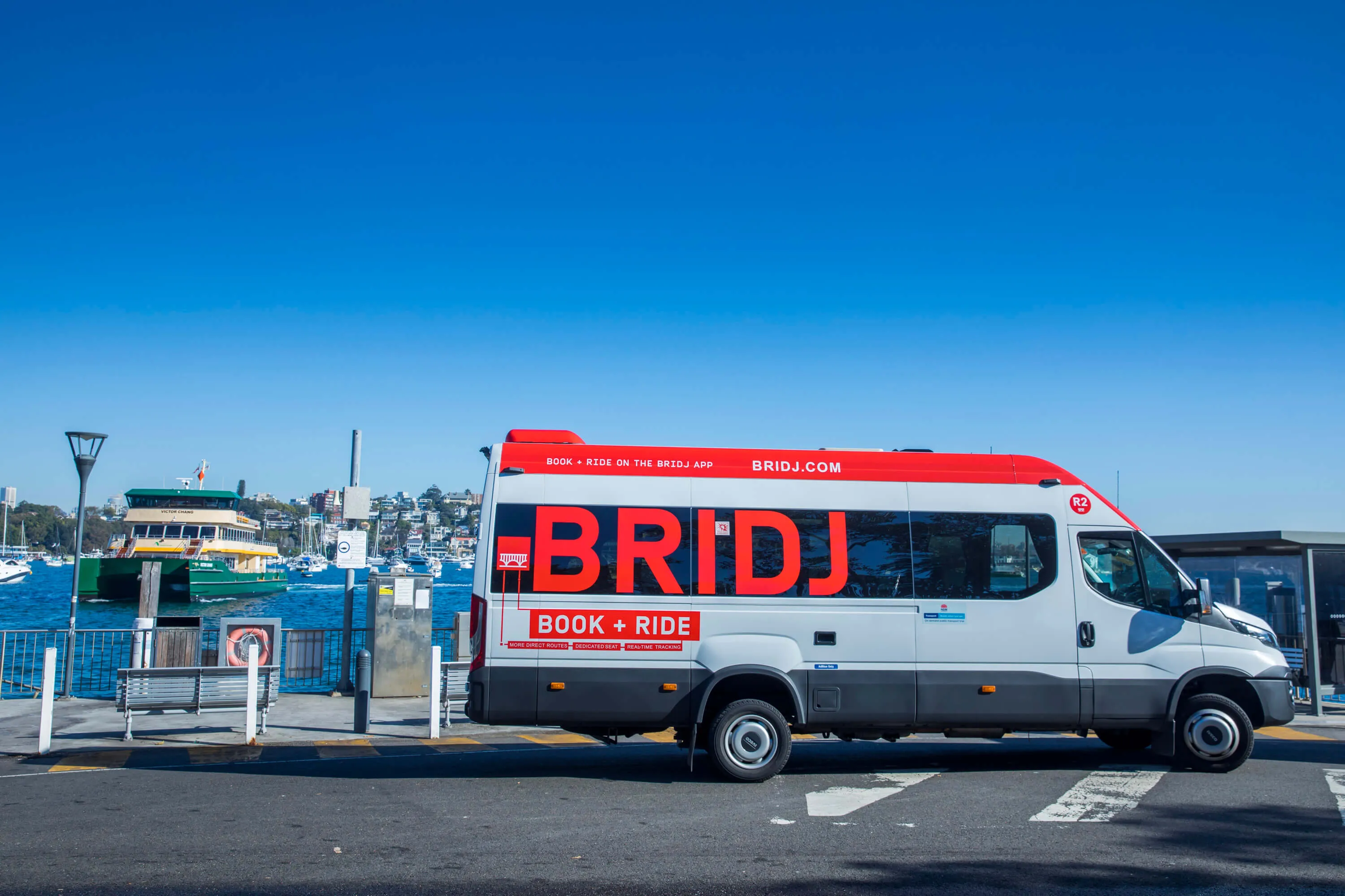 A white and grey "BRIDJ" van with red lettering, parked near a ferry terminal on a sunny day.