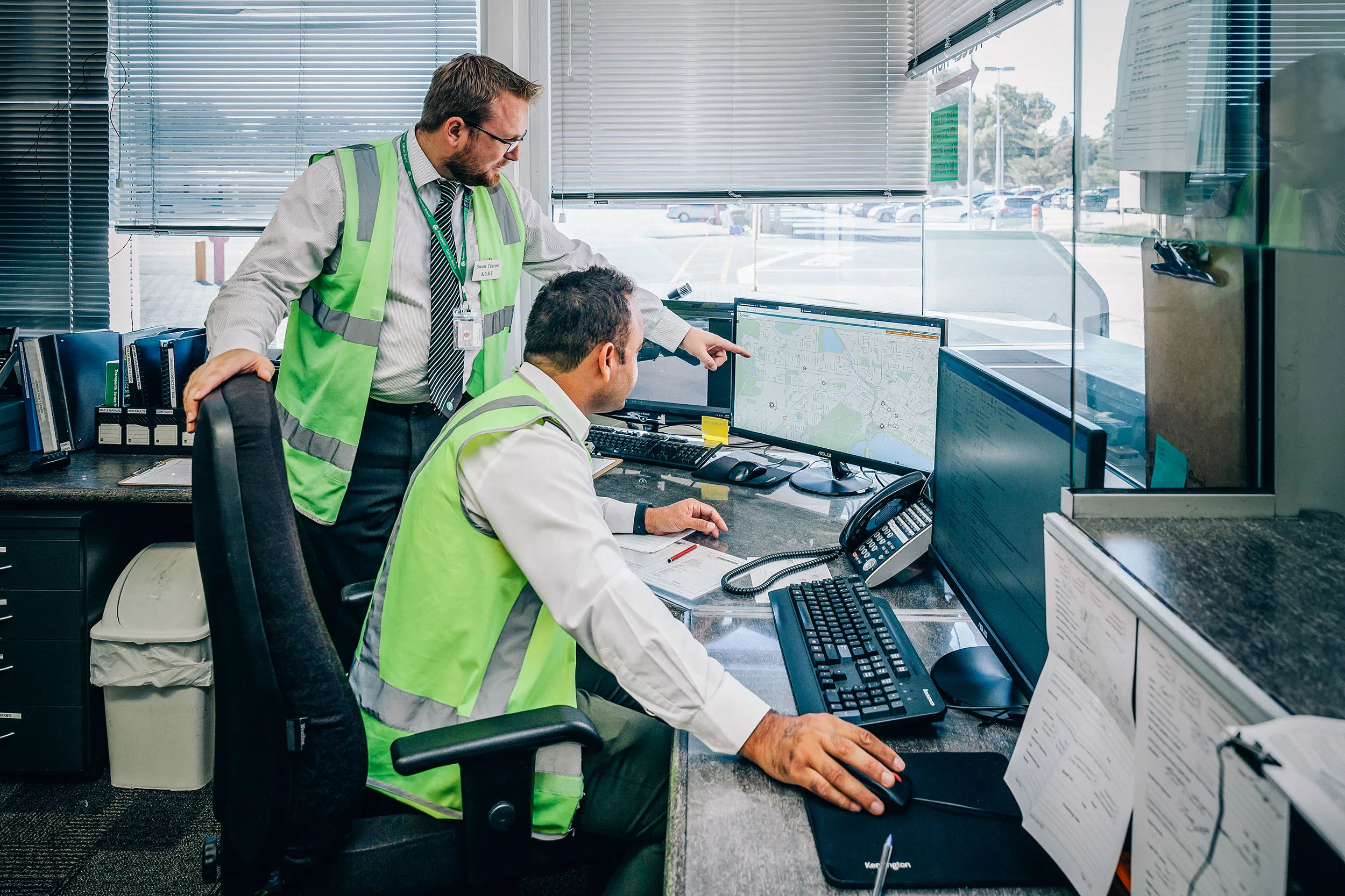 Two men in high-visibility vests looking at a computer screen displaying a map, likely for network planning.