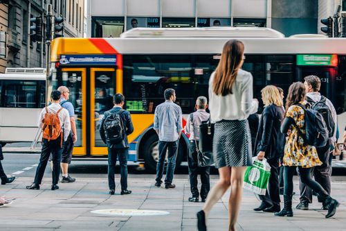 People waiting at a city bus stop with a yellow and white bus in the background.