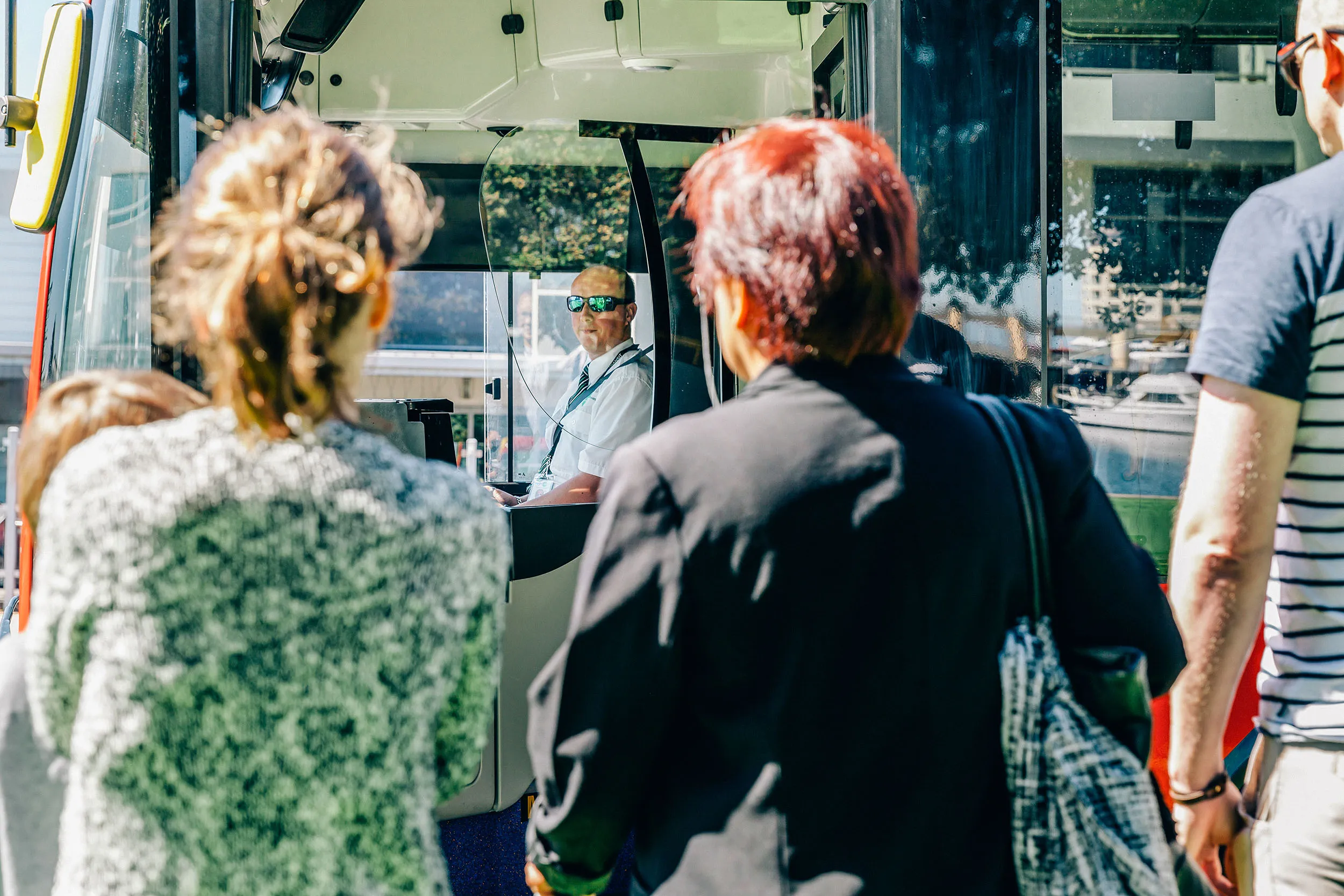 Passengers standing in a bus looking towards the smiling bus driver.