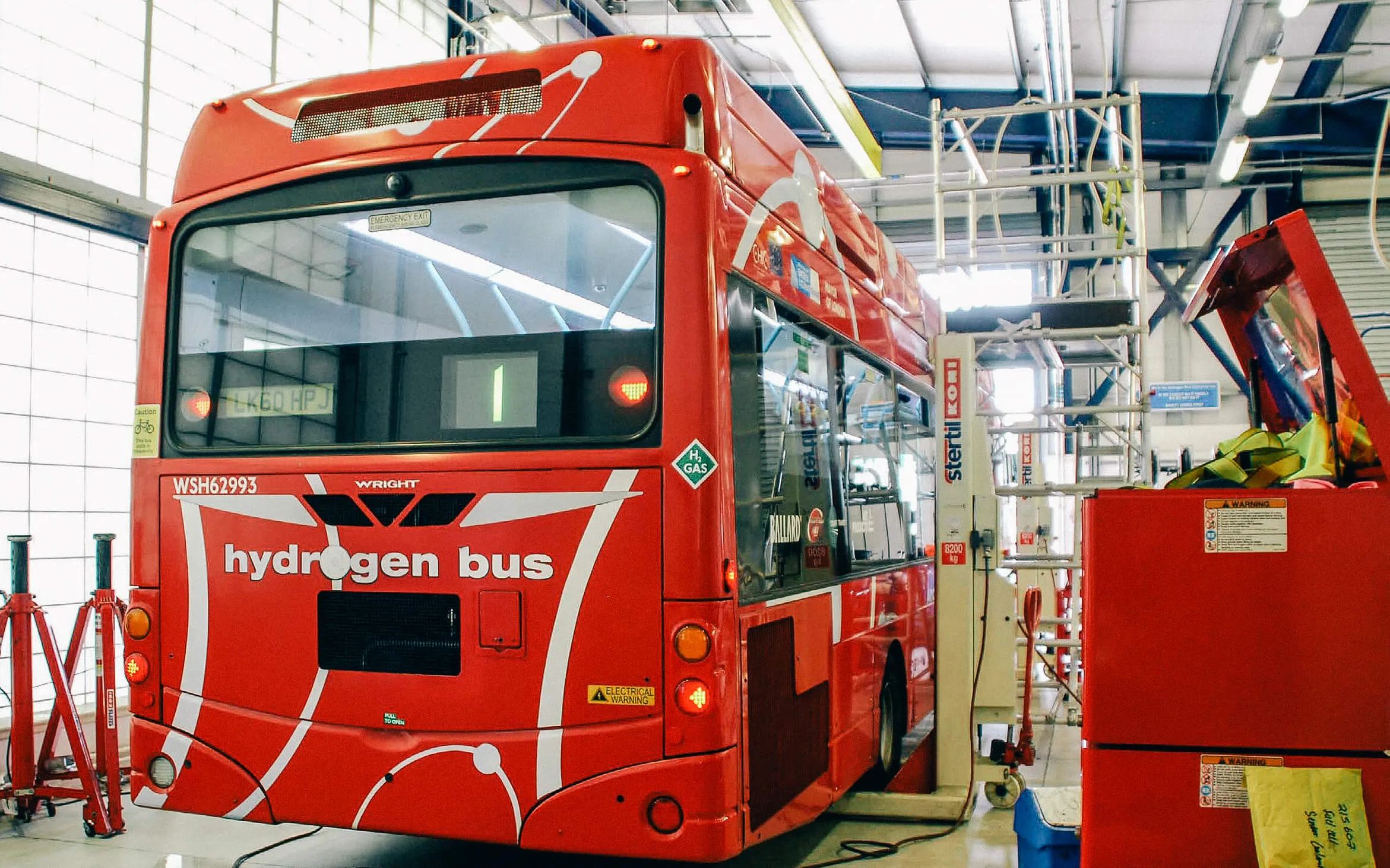 Rear view of a red "hydrogen bus" with white text, parked inside a workshop.