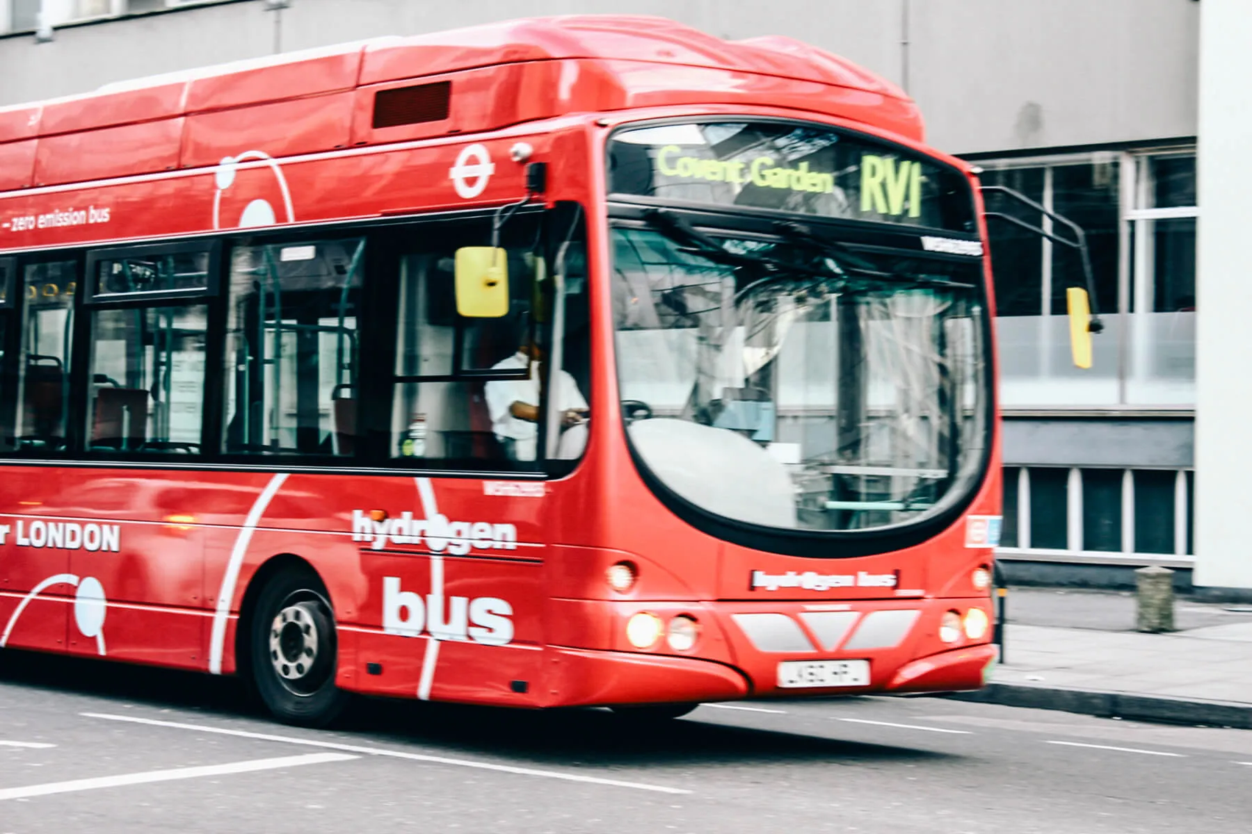A red "hydrogen bus" with "Covent Garden" displayed on its front, driving on a city street.