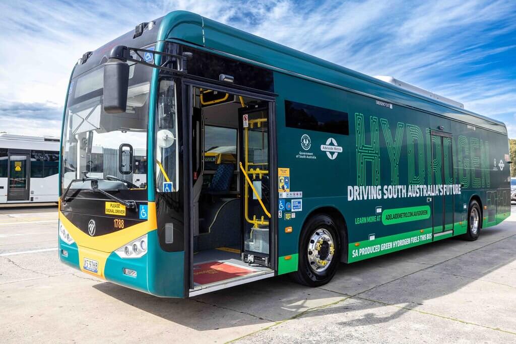 A large teal and yellow hydrogen-powered bus with its door open, displaying "Adelaide Metro" and "Driving South Australia's Future."