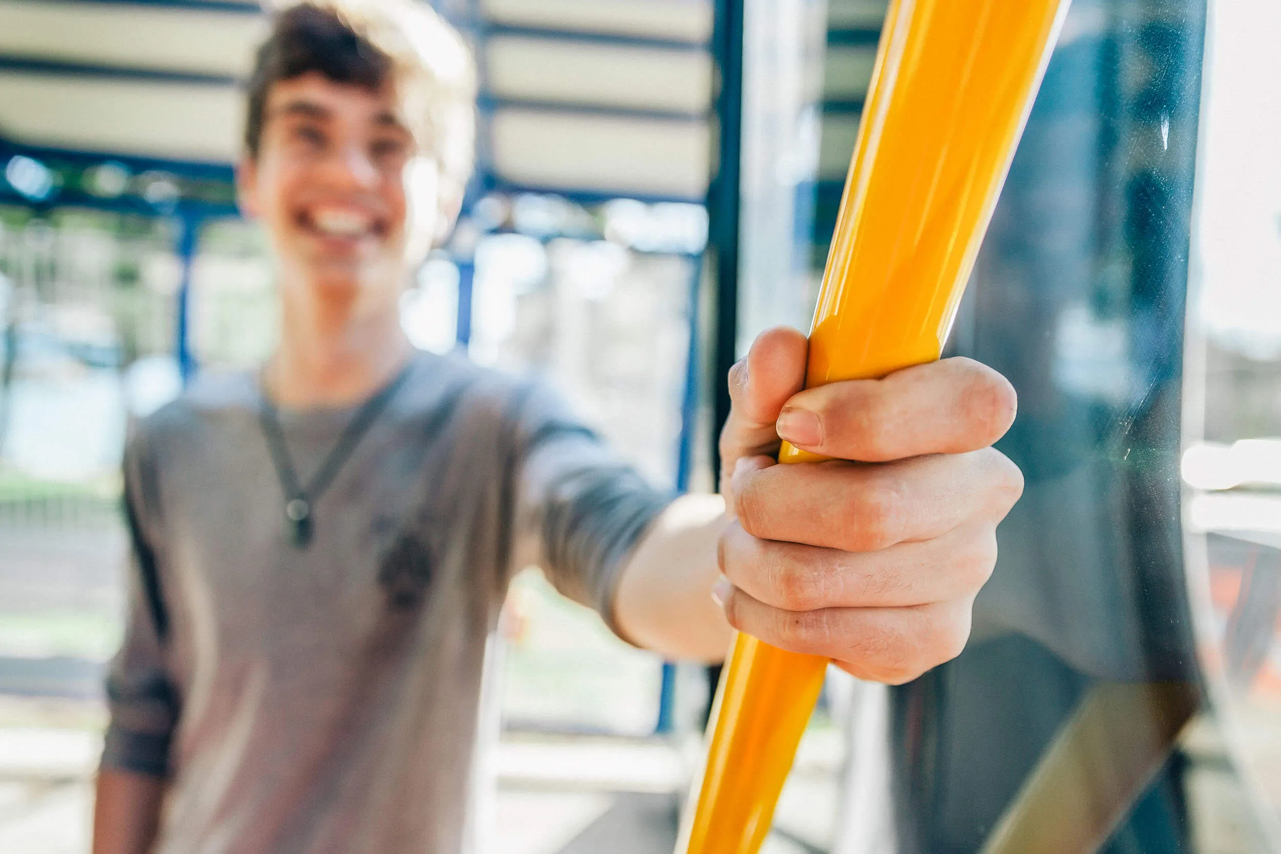 Hand gripping a yellow pole inside a bus with a smiling person in the background.