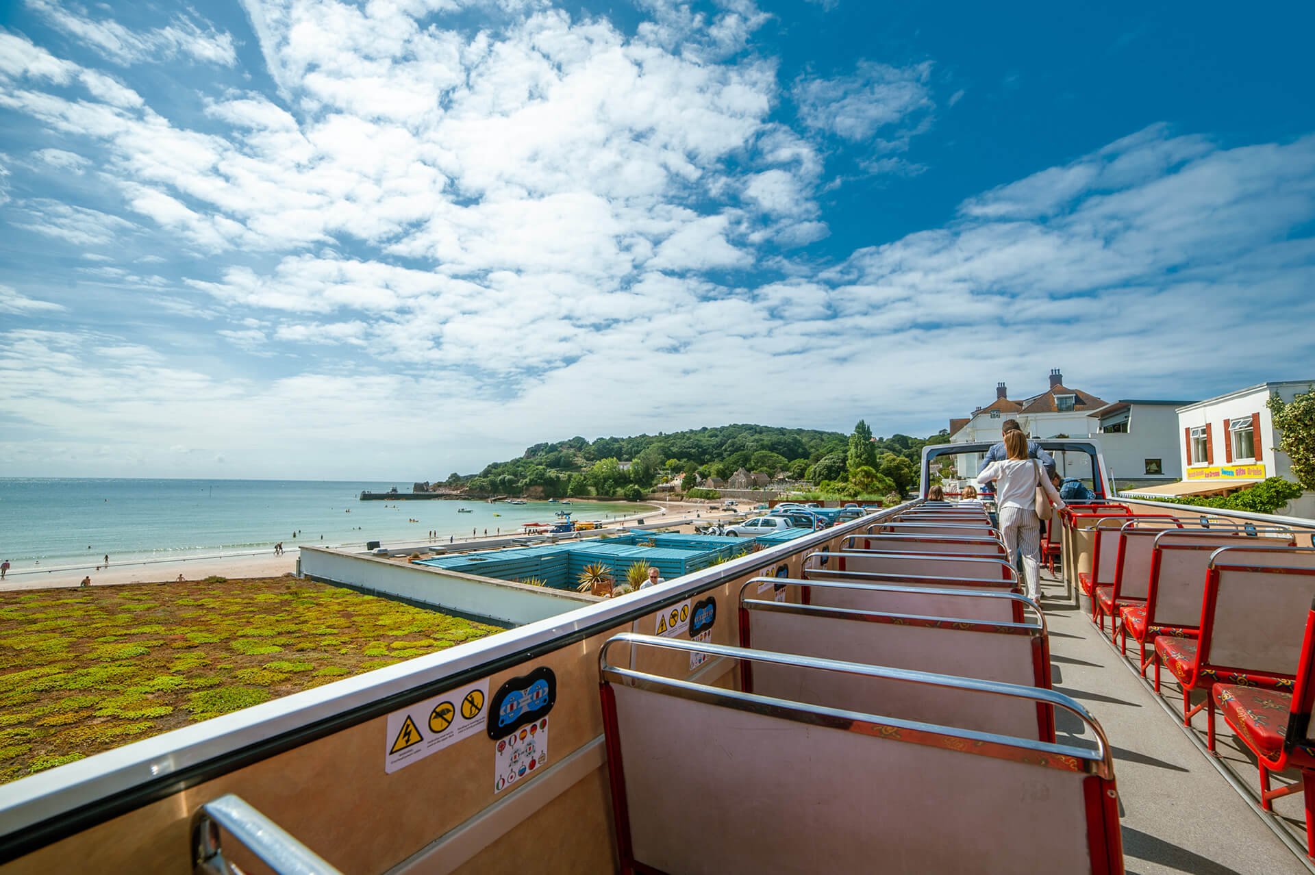 A scenic view from the upper deck of an open-top tour bus overlooking a beach, blue sky, and coastal landscape.