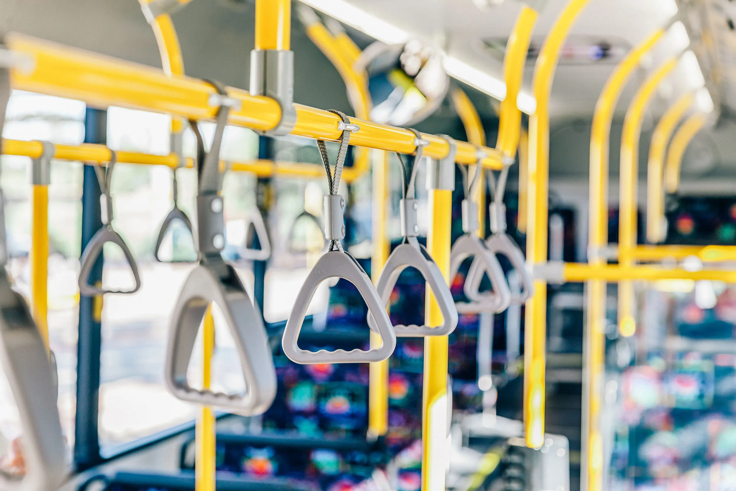 Close-up view of yellow overhead handrails and grey plastic hand grips inside a city bus.