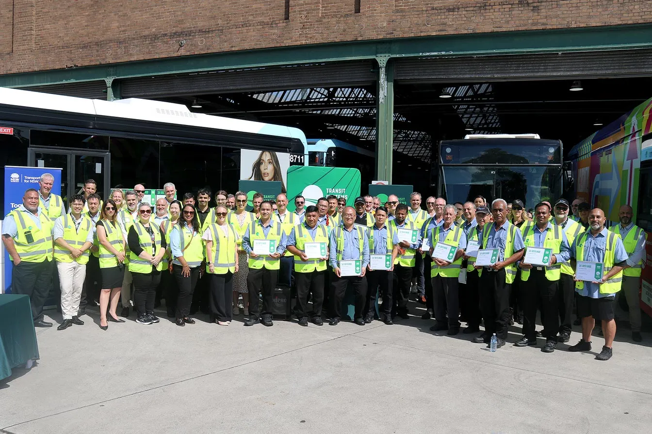 Group of 50 people stand in front of bus