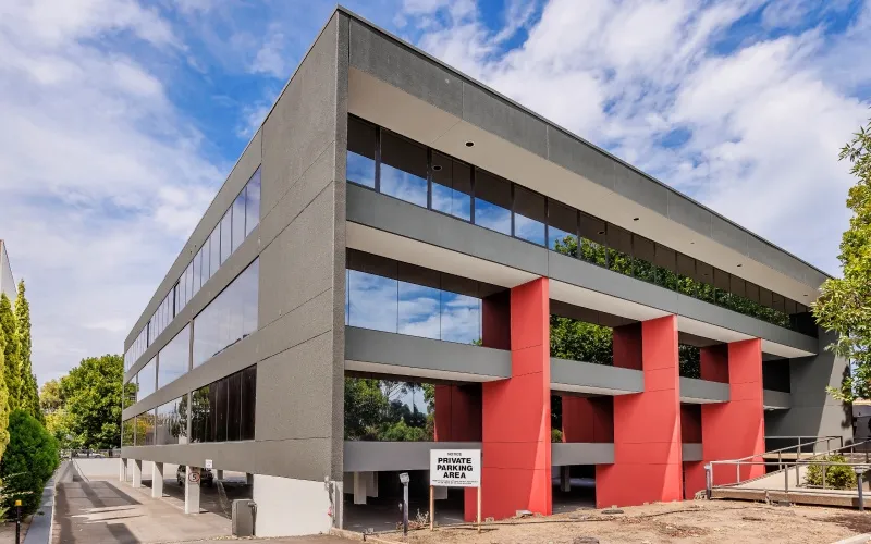 Modern commercial building with reflective windows, red columns, and a private parking area sign.