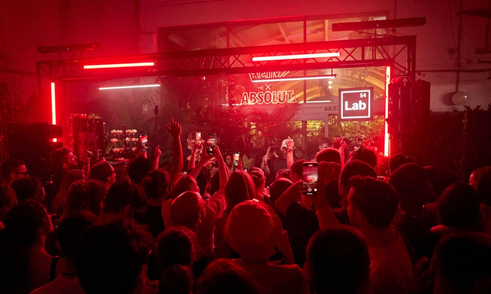 Crowd at a nighttime event under red lighting with illuminated signs